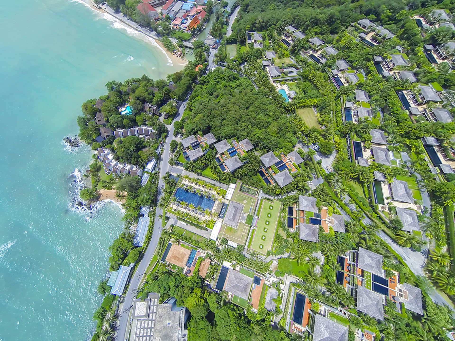 Luftaufnahme eines exklusiven Resortkomplexes an der Küste von Phuket: Villen mit Pools, tropischer Garten und Strand.
