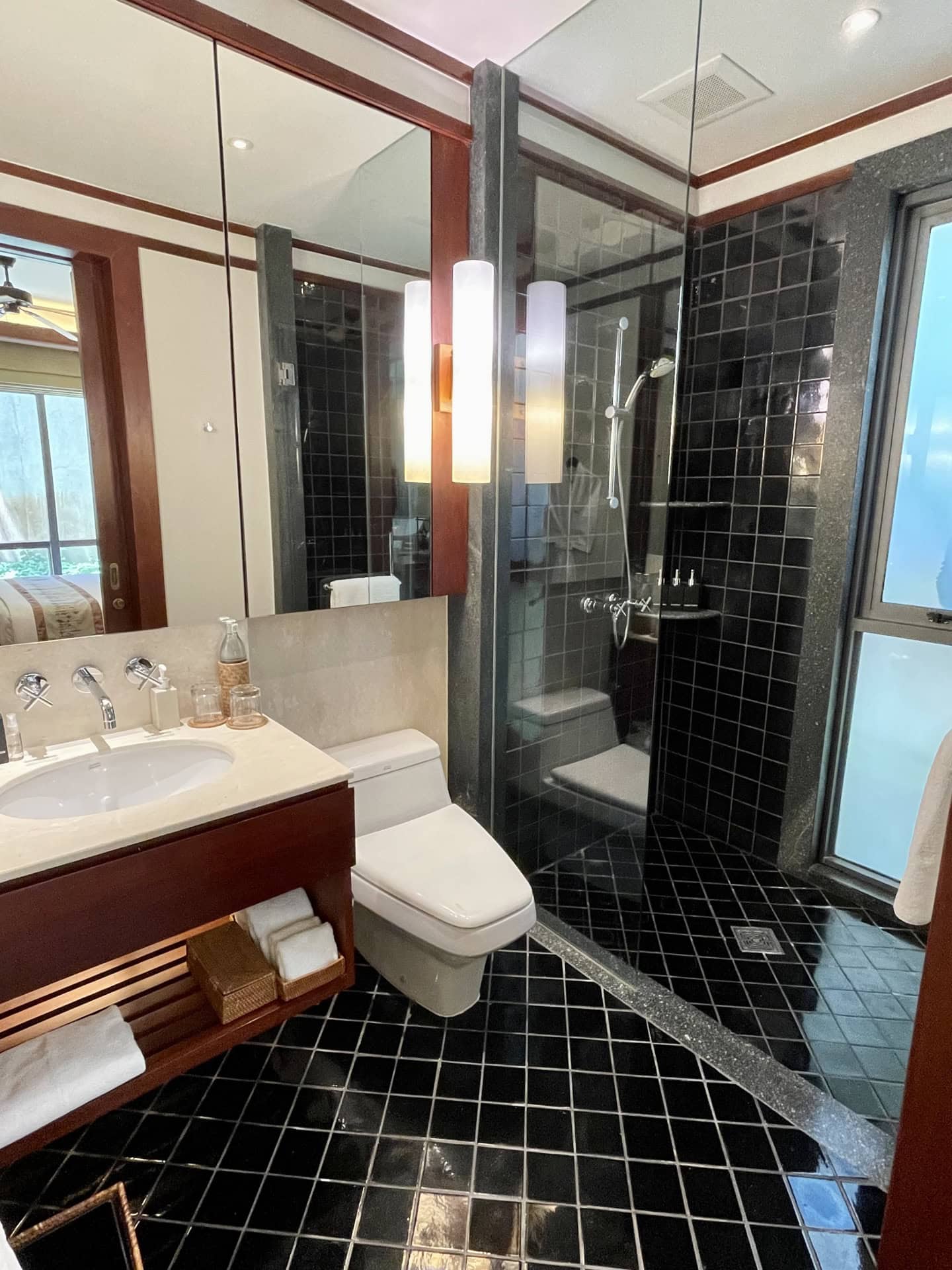 Modernes Badezimmer mit schwarzen Fliesen, Glasduschkabine und Holzmöbeln in einem Apartment auf Phuket