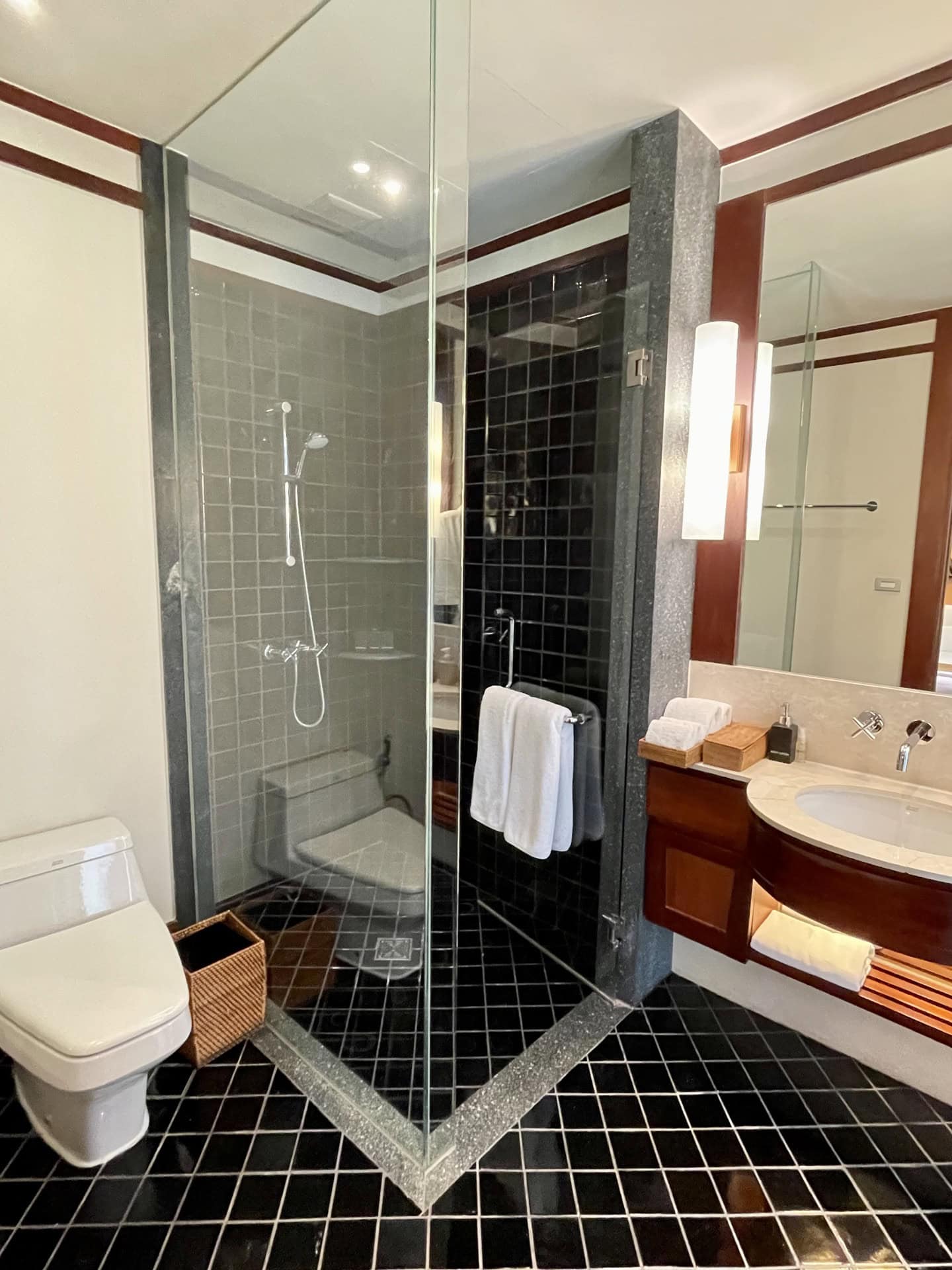 Modernes Badezimmer mit Duschkabine, schwarzer Fliesenverkleidung und Holzmöbeln in den Apartments, Phuket