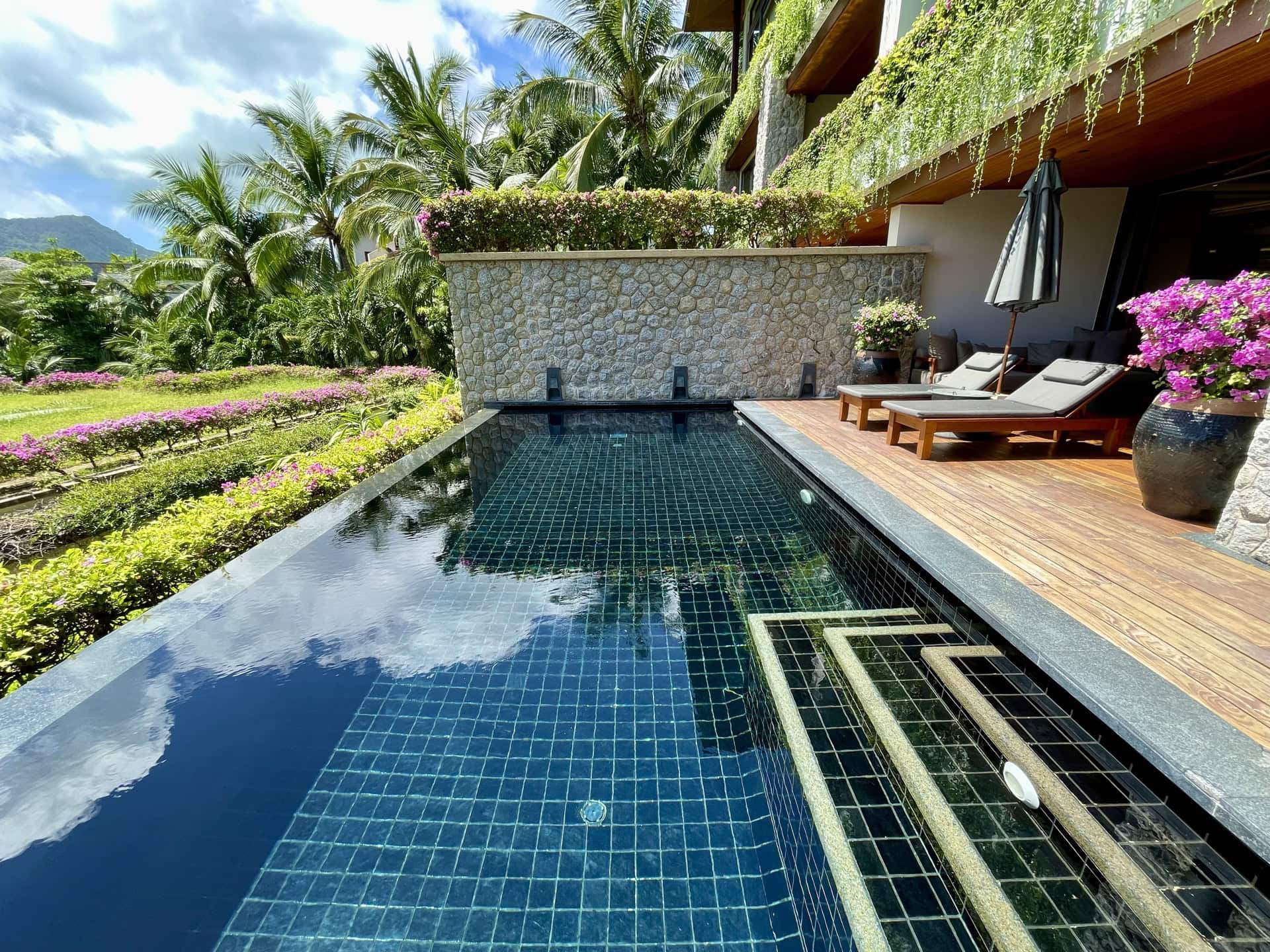 Privater Pool mit dunklen Fliesen, Holzterrasse, Liegestühlen und tropischem Garten in exklusiven Apartments auf Phuket.