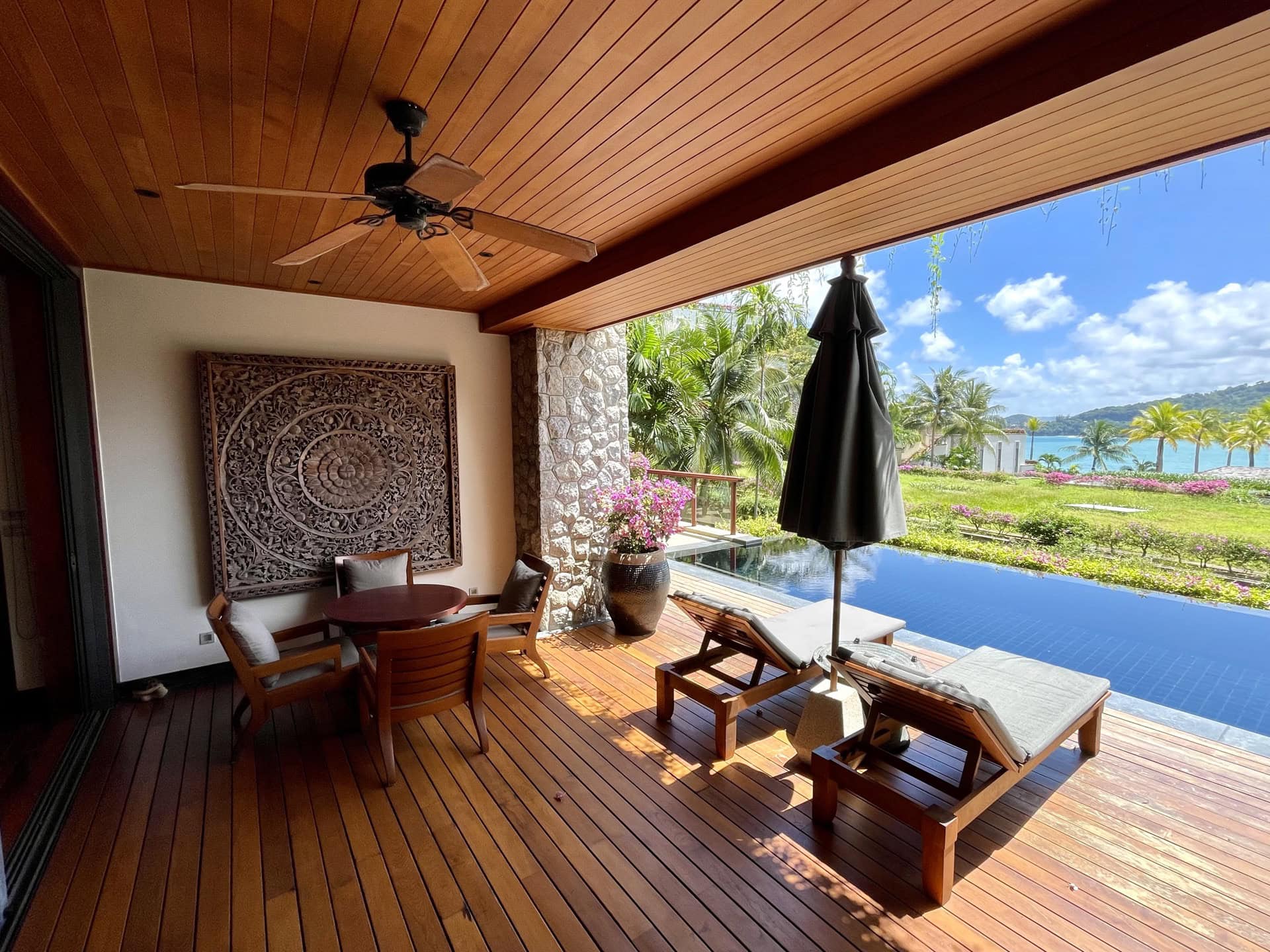 Terrasse der Apartments auf Phuket mit Holzdeck, privatem Pool, Sonnenliegen und Blick auf das Meer und den Garten.