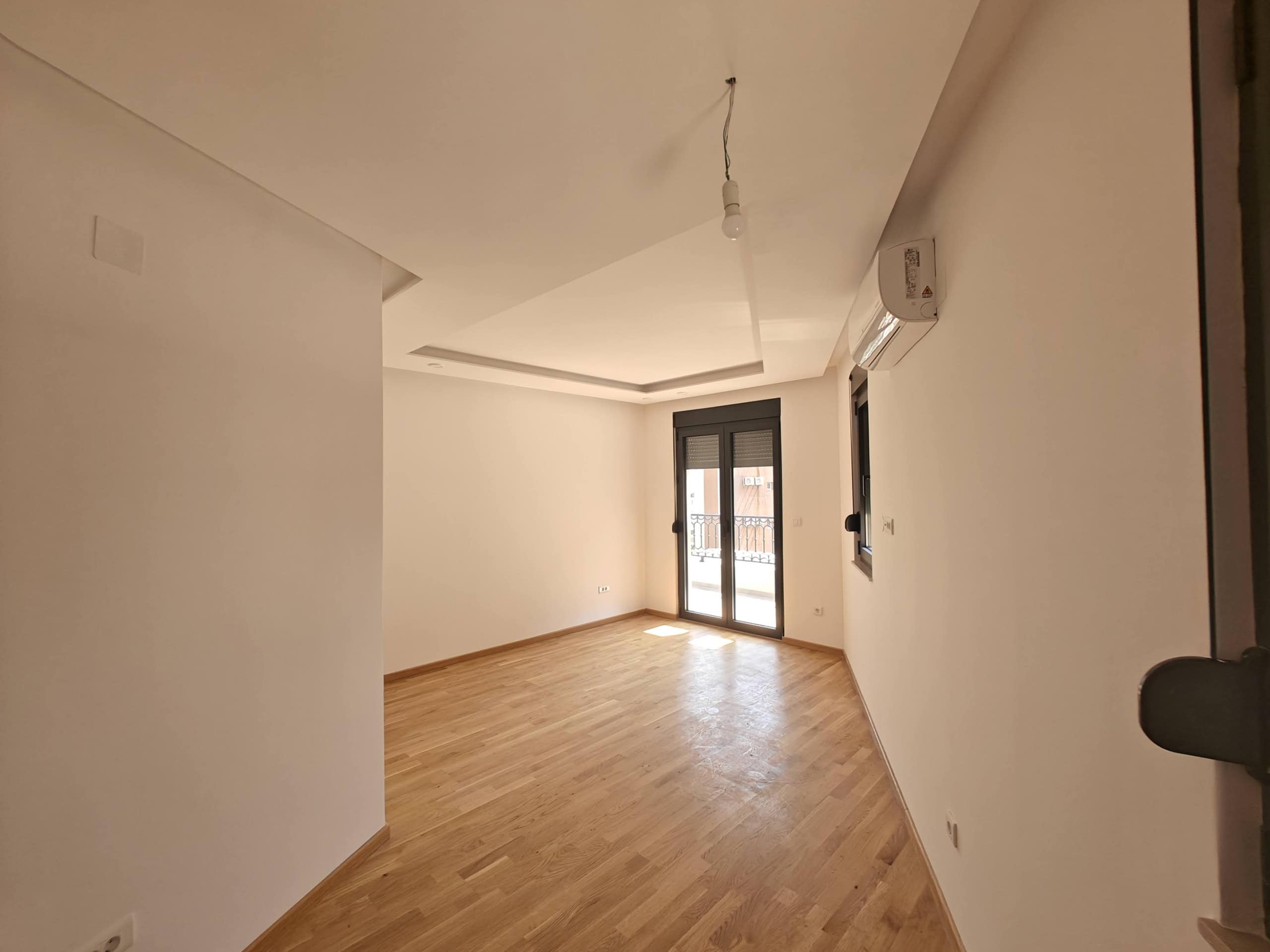 Svetao dnevni boravak sa parketom, klima-uređajem i izlazom na balkon u novom stanu, Budva, Crna Gora.