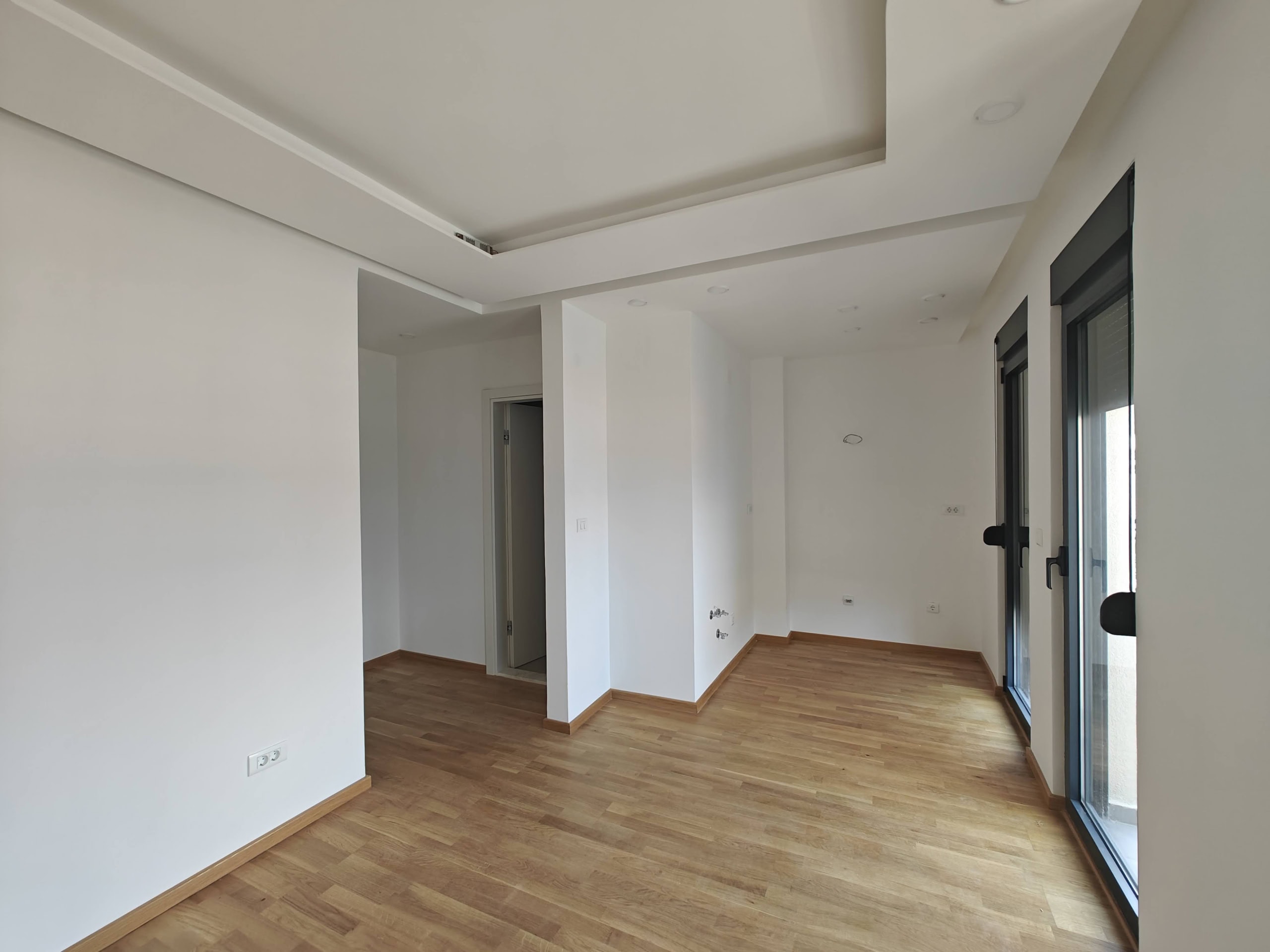 Svetla dnevna soba sa parketom i panoramskim prozorima u novom stanu u Budvi, Crna Gora. Moderan enterijer.