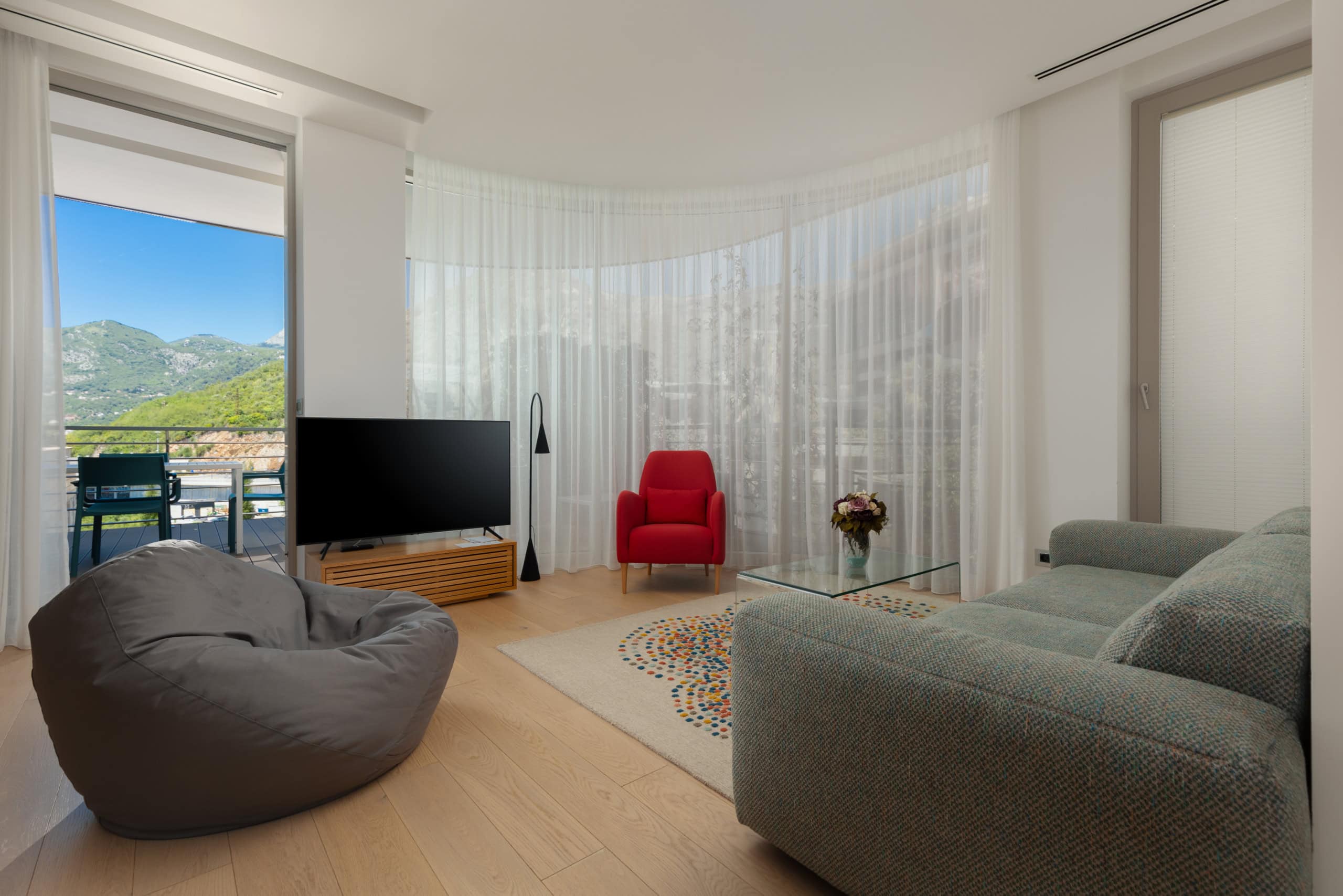 Modernes Wohnzimmer im ЖК Будva, Montenegro: Panoramafenster, Bergblick, stilvolle Möbel und Zugang zur Terrasse.