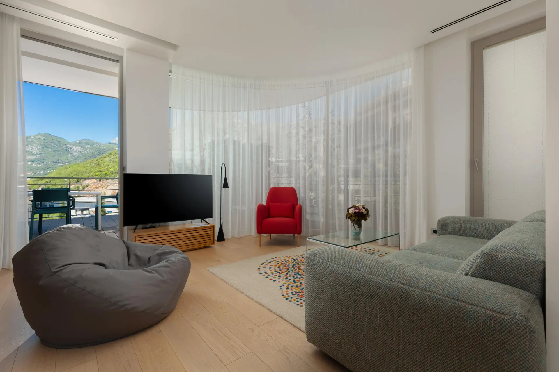 Modernes Wohnzimmer im ЖК Будva, Montenegro: Panoramafenster, Bergblick, stilvolle Möbel und Zugang zur Terrasse.