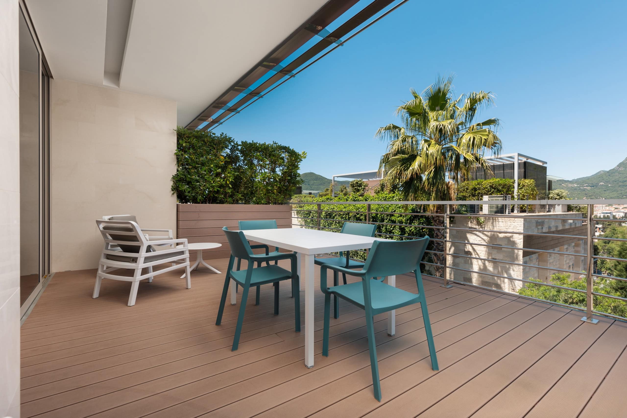 Terrasse mit Möbeln in einer Wohnanlage in Budva, Montenegro: Holzdeck, Essbereich und Bergblick.