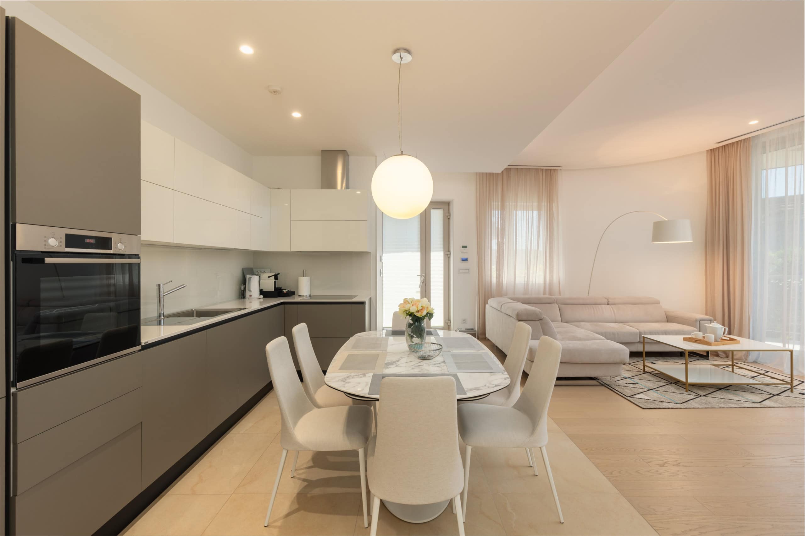 Moderne Wohnküche mit Essbereich in einer Wohnanlage in Budva, Montenegro: helles Interieur, weiche Möbel und Geräte.