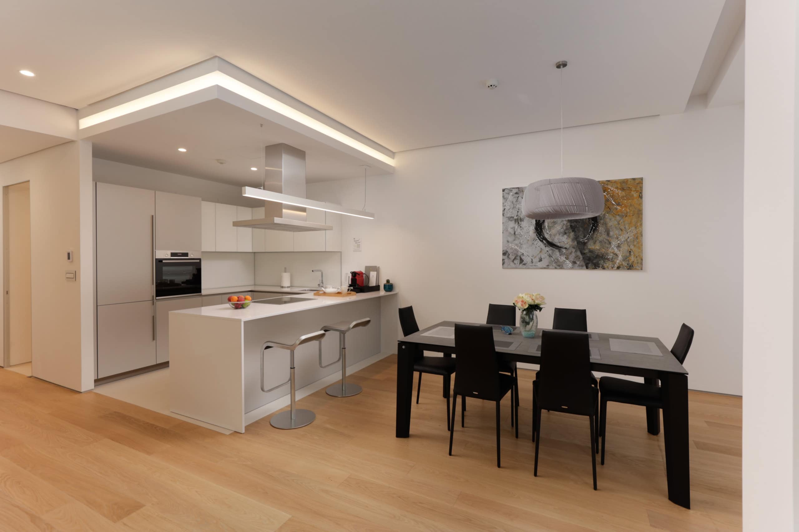 Moderne Wohnküche in der Wohnanlage Budva, Montenegro: weiße Möbel, Kochinsel mit Barhockern und Essbereich.