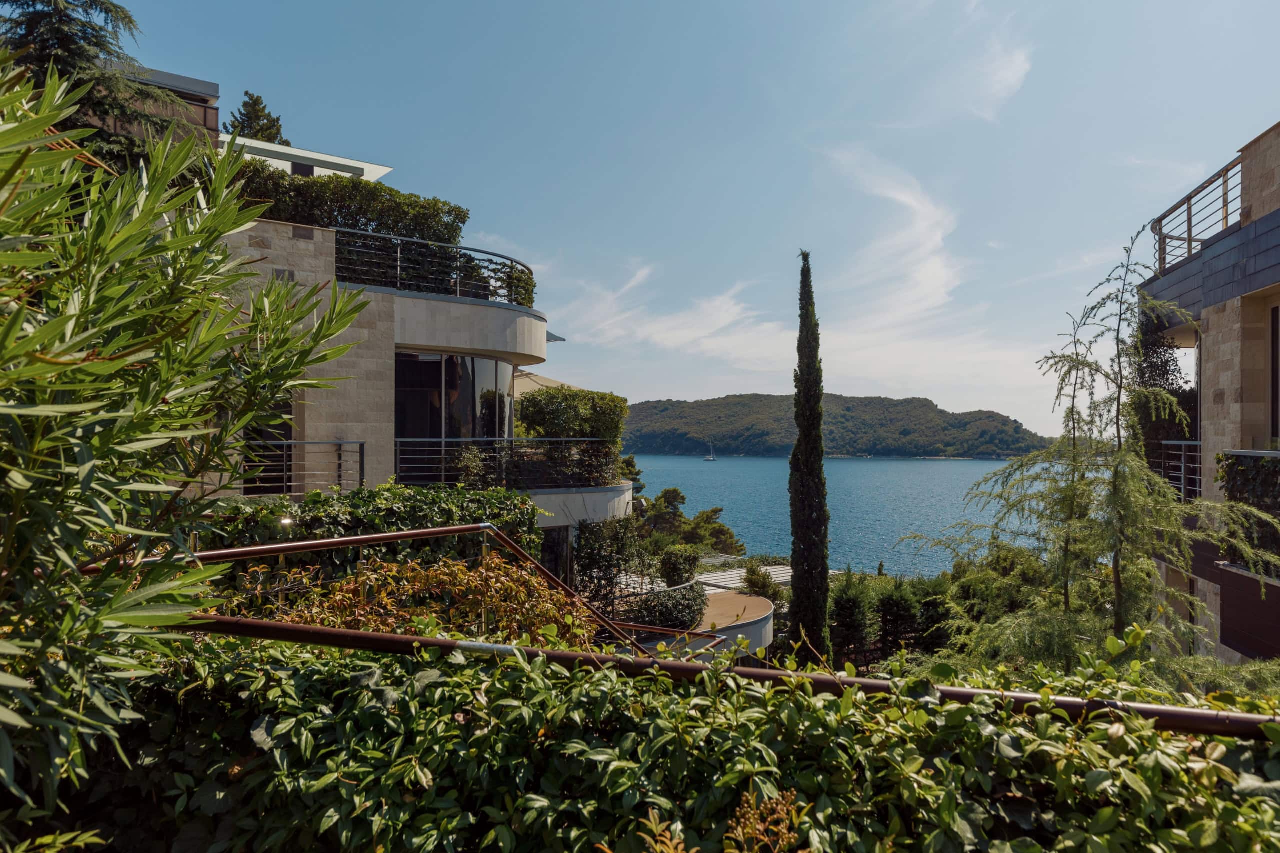 Moderne Villa mit Terrassen und Panoramablick auf das Meer in Budva, Montenegro, umgeben von Grün und Zypressen.