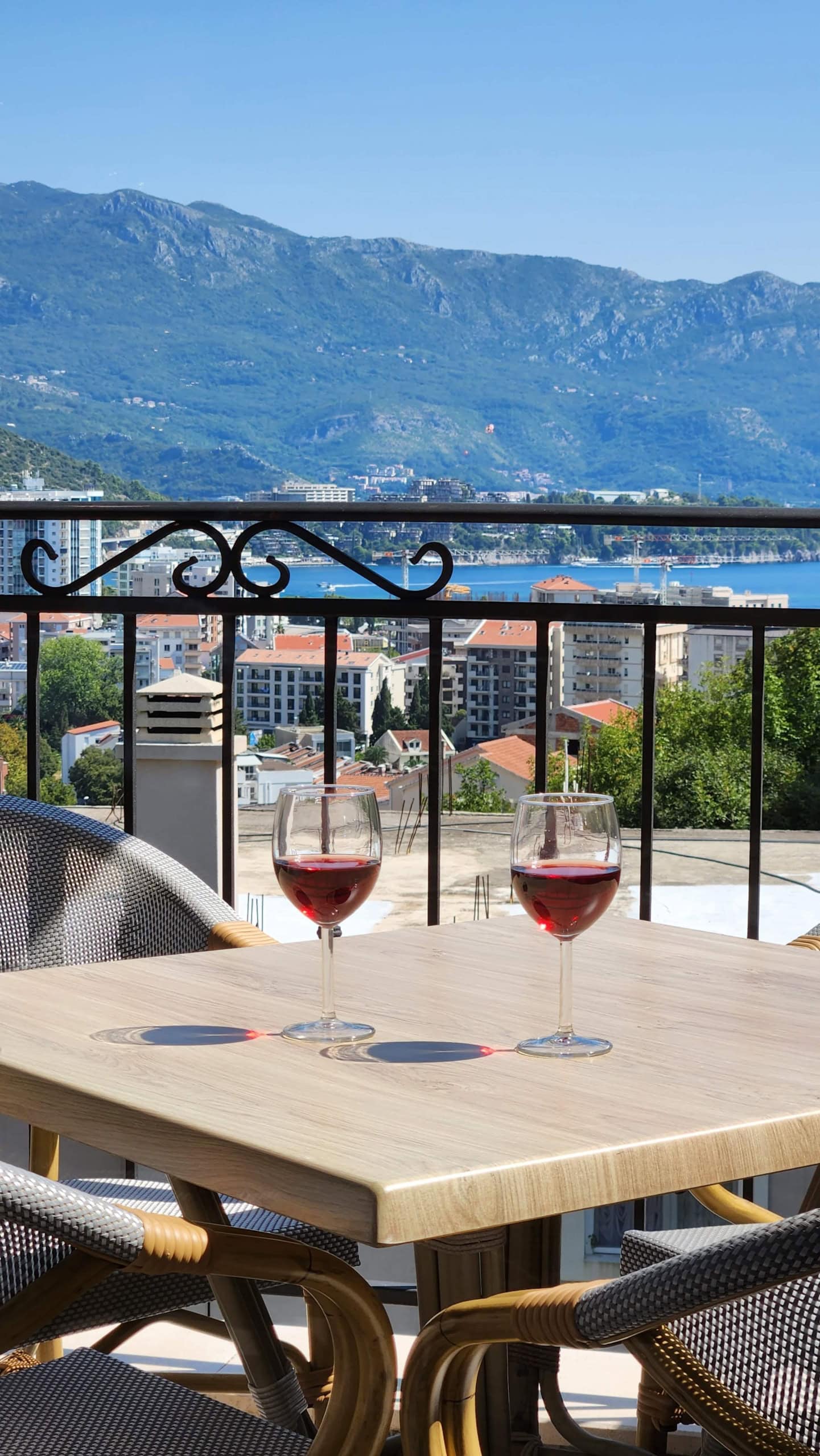 Two glasses of wine on the balcony of an apartment in Budva, Montenegro, with a panoramic view of the sea and mountains.