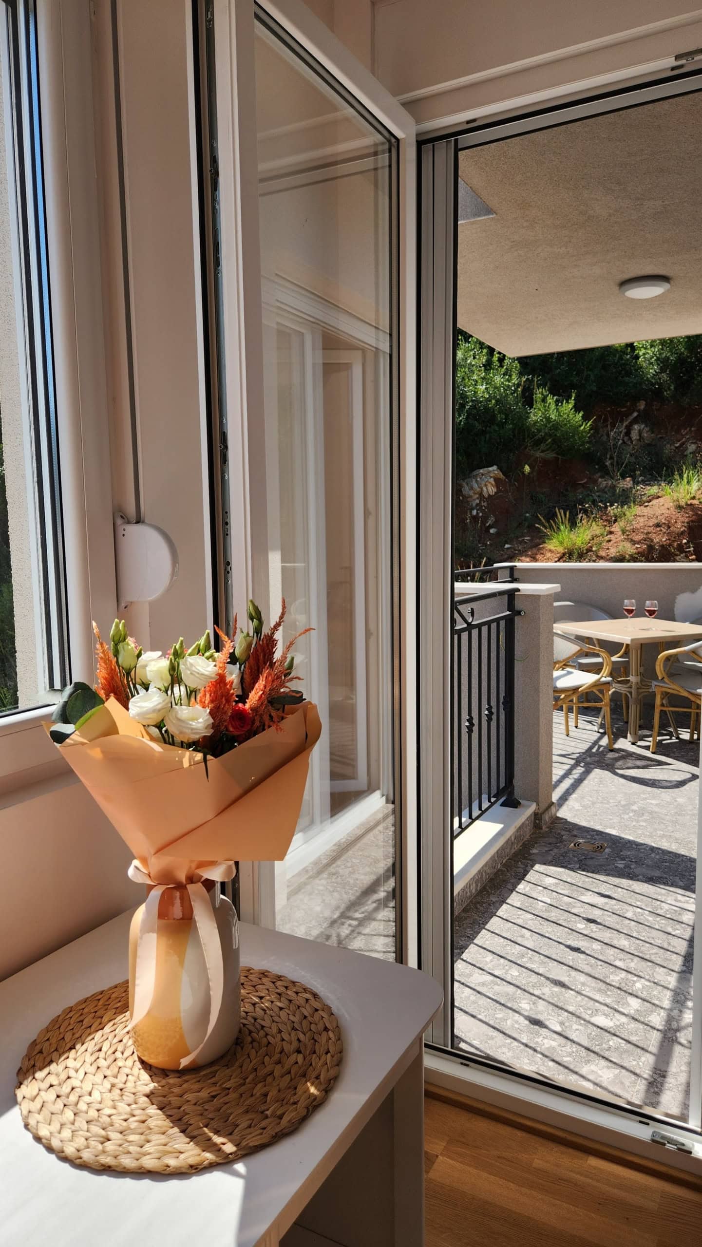 A bouquet of flowers on a table and access to a terrace with patio furniture in an apartment in Budva, Montenegro.