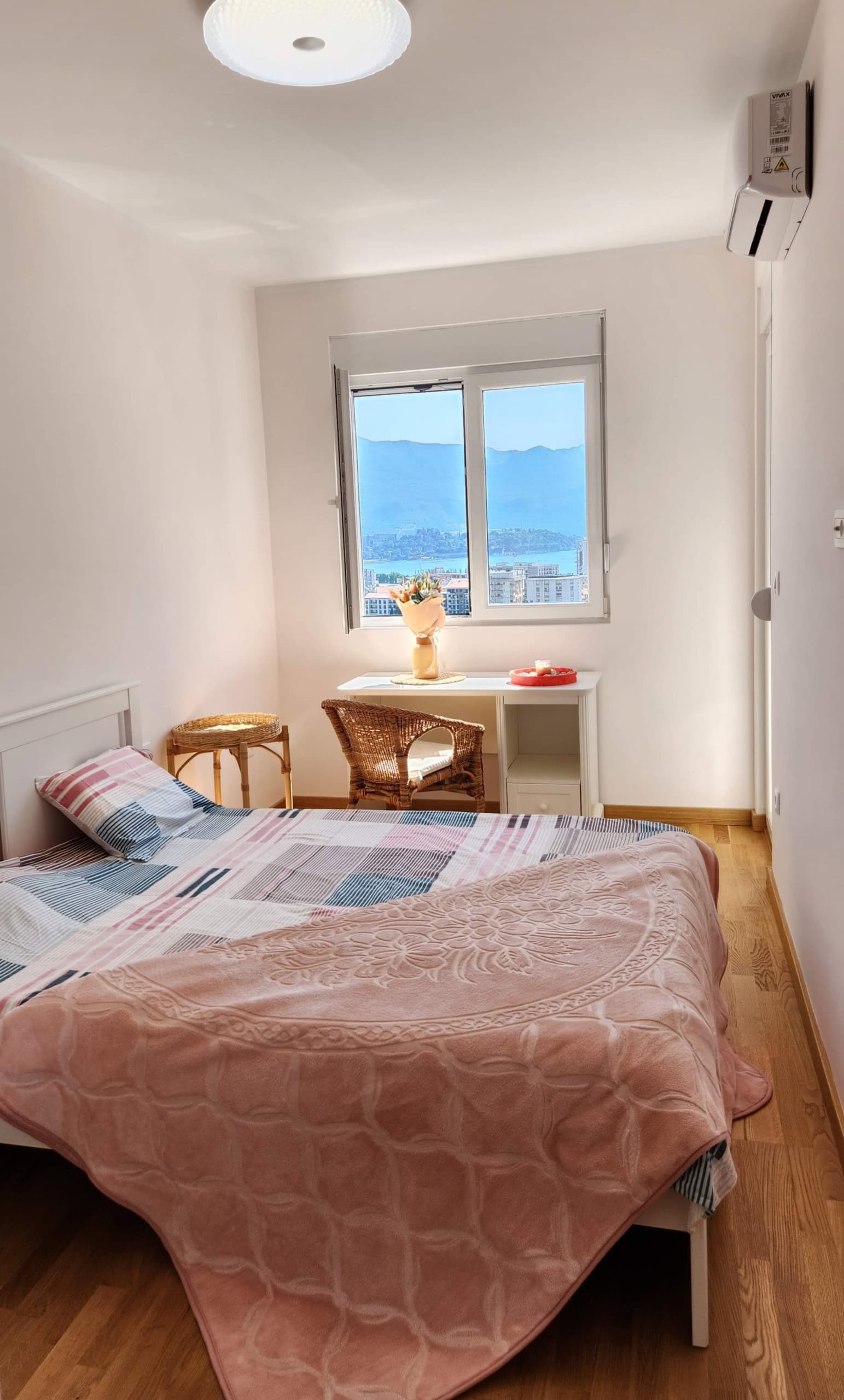 Cozy bedroom with a sea and mountain view in a Budva apartment, Montenegro: double bed, desk, and parquet flooring.
