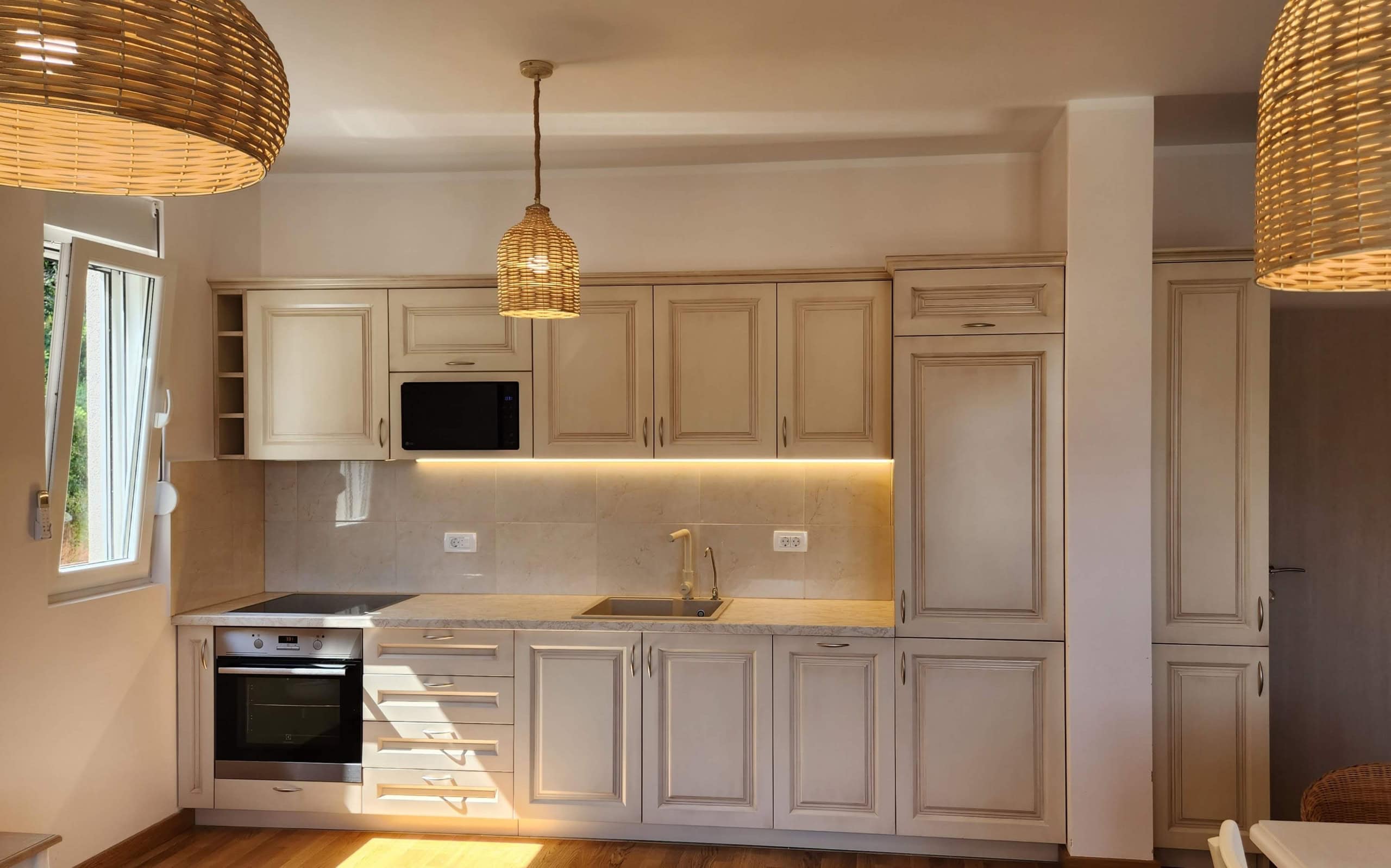 Modern bright kitchen in a Budva apartment, Montenegro: built-in appliances, woven pendant lights, and stylish design.