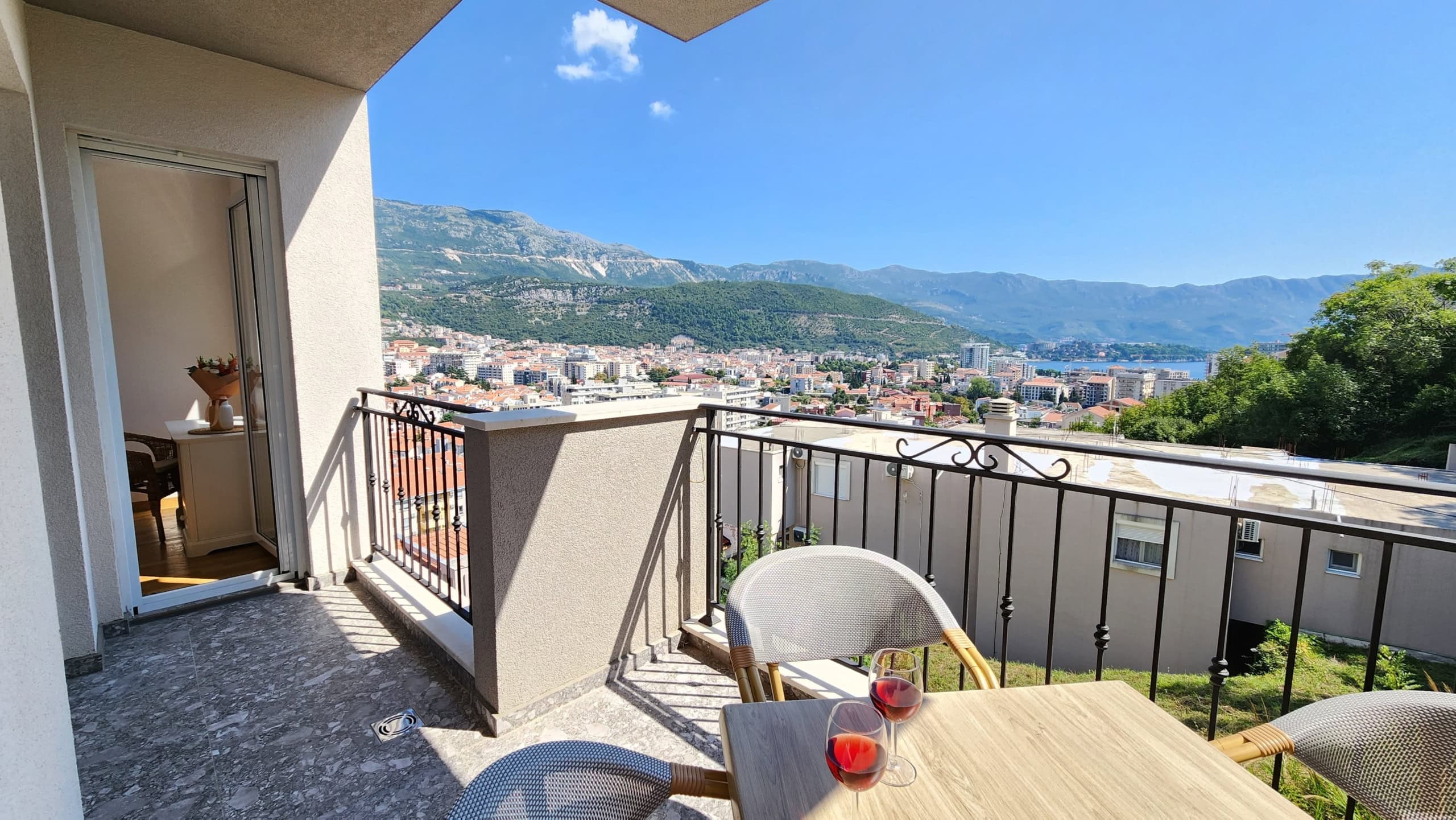 Balcony with furniture and a view of the city of Budva, mountains, and the sea in Montenegro. Cozy apartment terrace with a panoramic landscape.