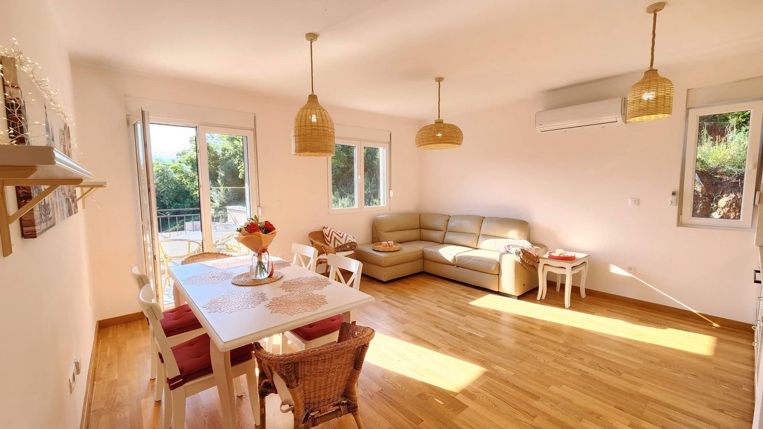 Bright living room with a leather sofa and dining area in a Budva, Montenegro apartment, featuring parquet flooring and balcony access.