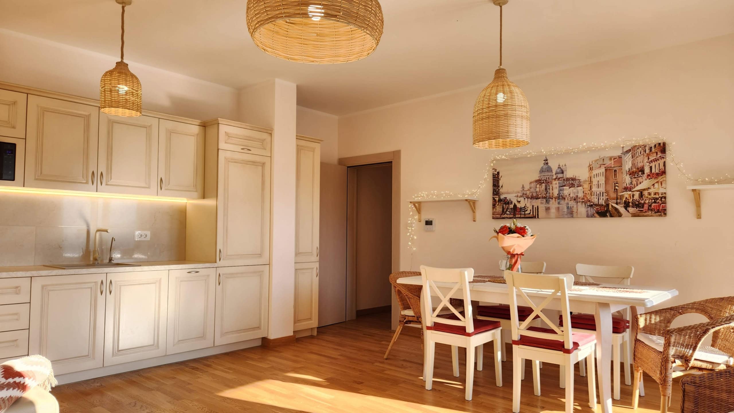 Bright kitchen-dining room in a Budva apartment, Montenegro: beige cabinetry, wicker pendant lights, and a dining area.