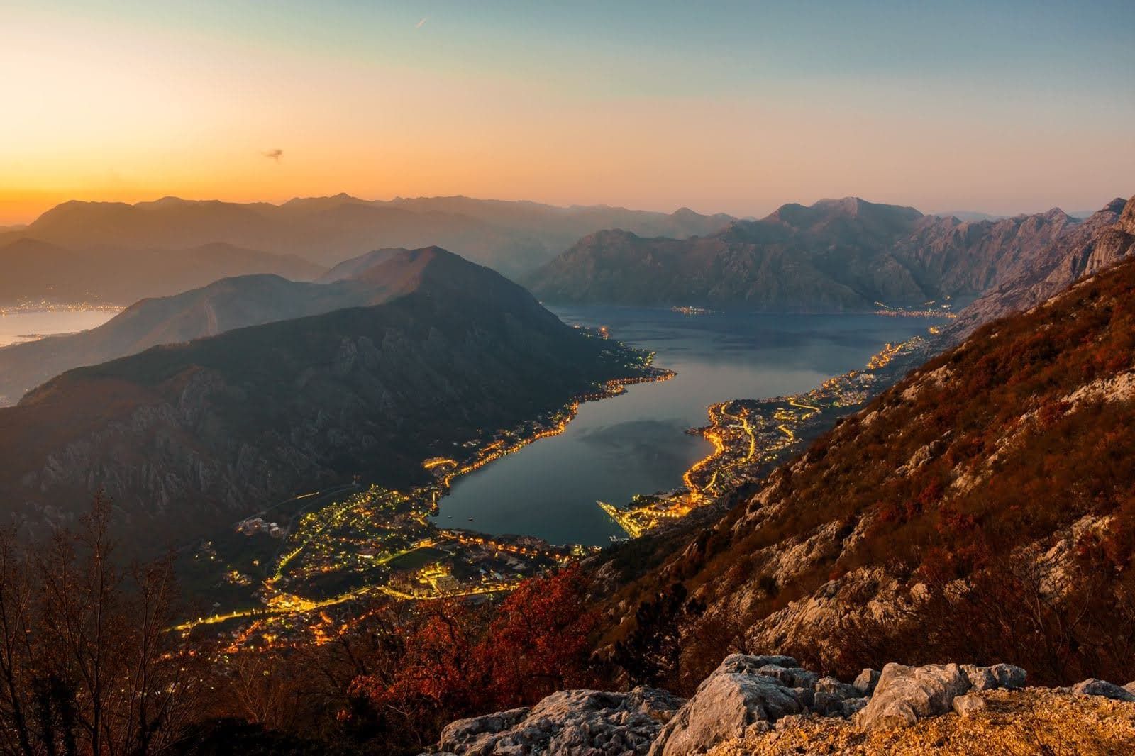 Karadağ'da gün batımında Kotor Körfezi ve Prčanj şehrinin panoramik manzarası, dağdan kıyının gece ışıkları görünümü.