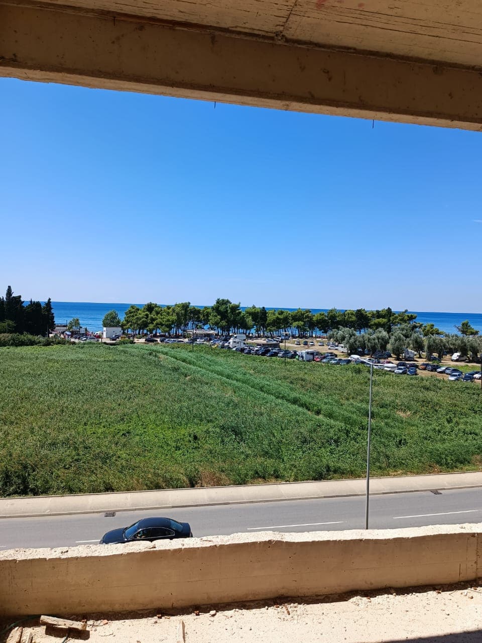 Vue depuis le balcon d’un complexe résidentiel à Shushan, Monténégro : panorama sur la mer, une zone verte et la route.