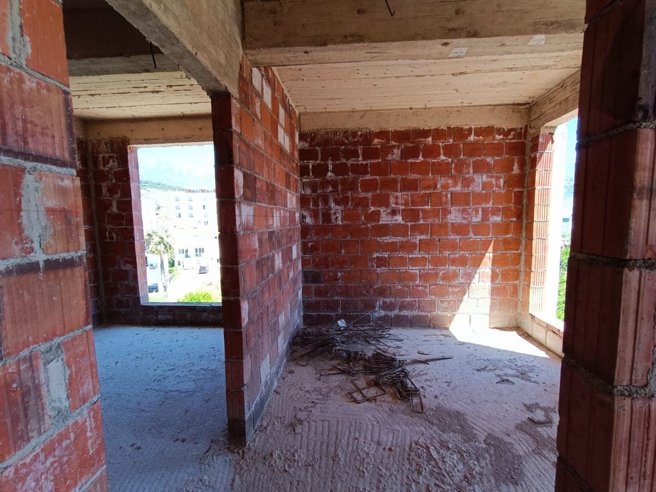 Appartement en construction dans le ЖК Шушань, Monténégro : murs en briques sans finition, dalles en béton et vue depuis les fenêtres.