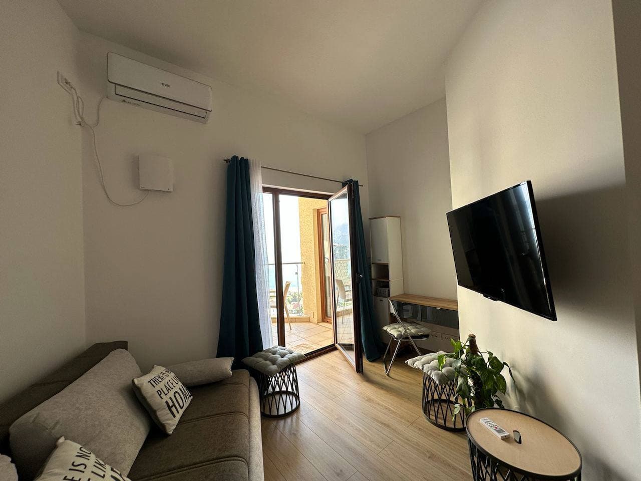 Udobna dnevna soba sa izlazom na balkon u stanu u Bečićima, Crna Gora: sofa, TV, klima uređaj i svetla završna obrada.