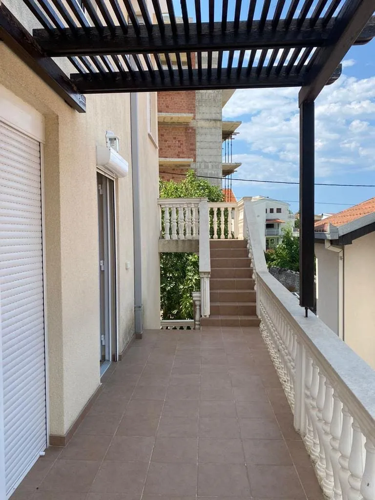 Geniş tente ve merdivenli teras, Dobra Voda, Karadağ. Komşu binalar ve yeşillik manzarası.