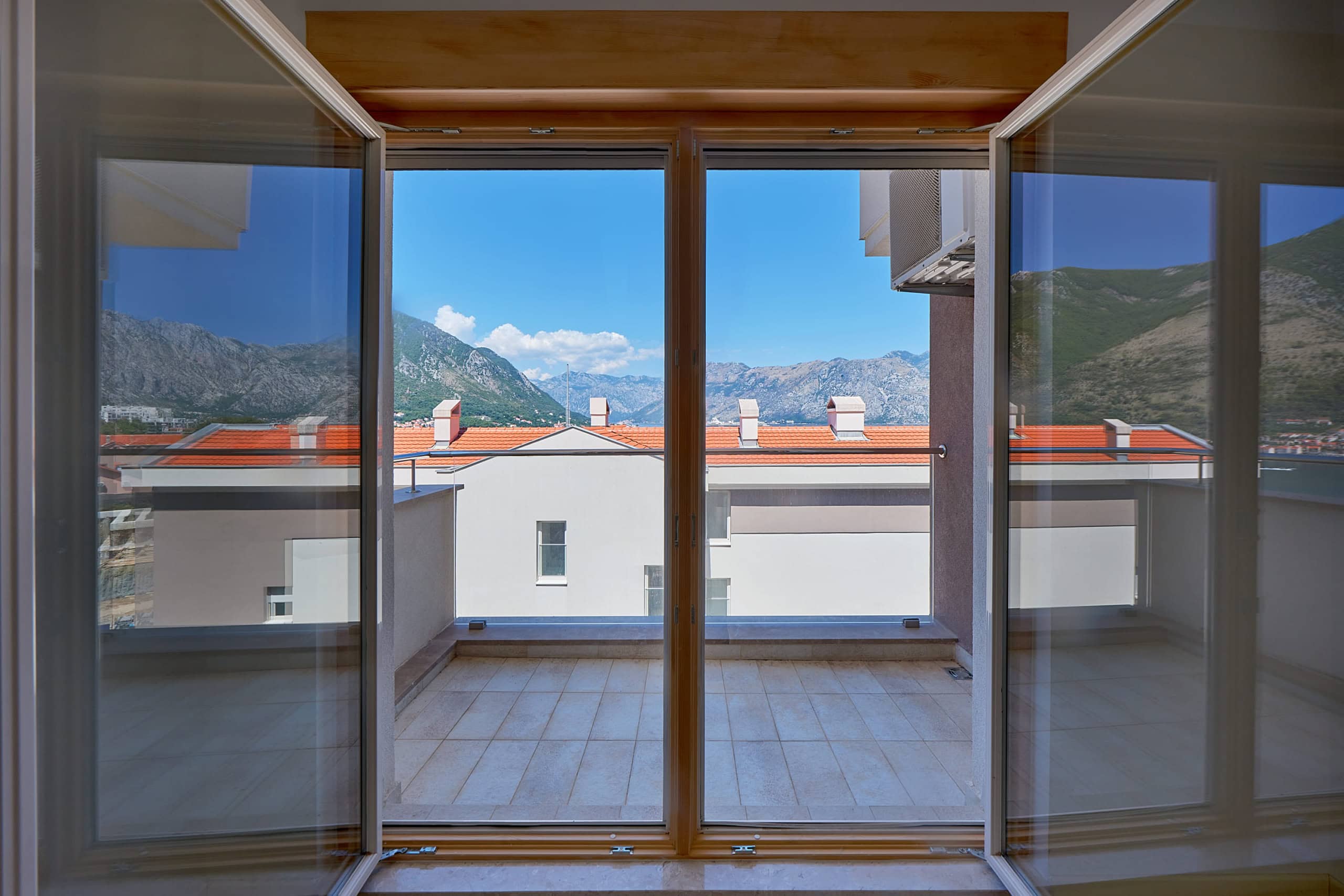 View from the apartment balcony in Dobrota, Montenegro: a panorama of mountains and the bay, modern houses with tiled roofs.