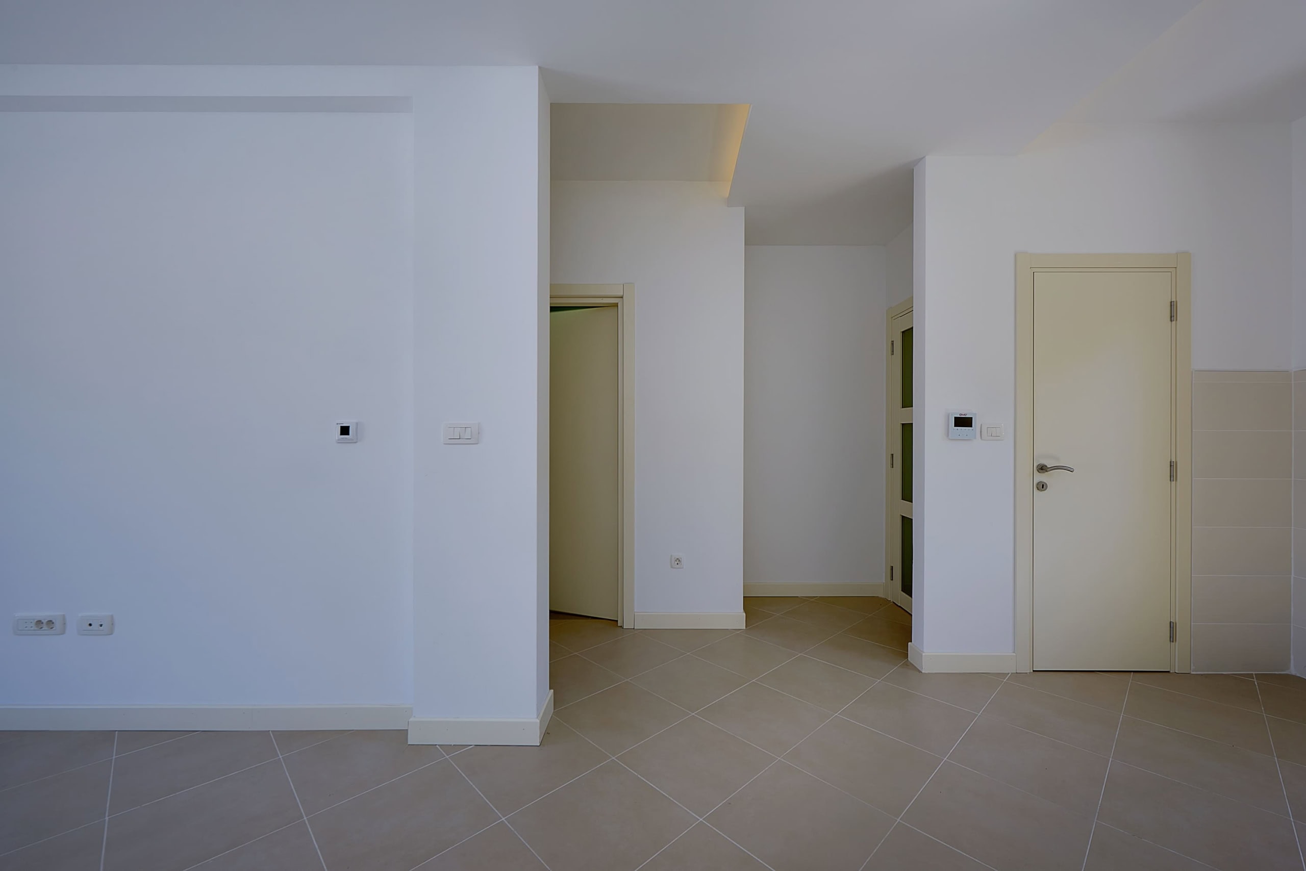 Bright living room with white walls and beige tile in an apartment in Dobrota, Montenegro. Interior doors and doorways.