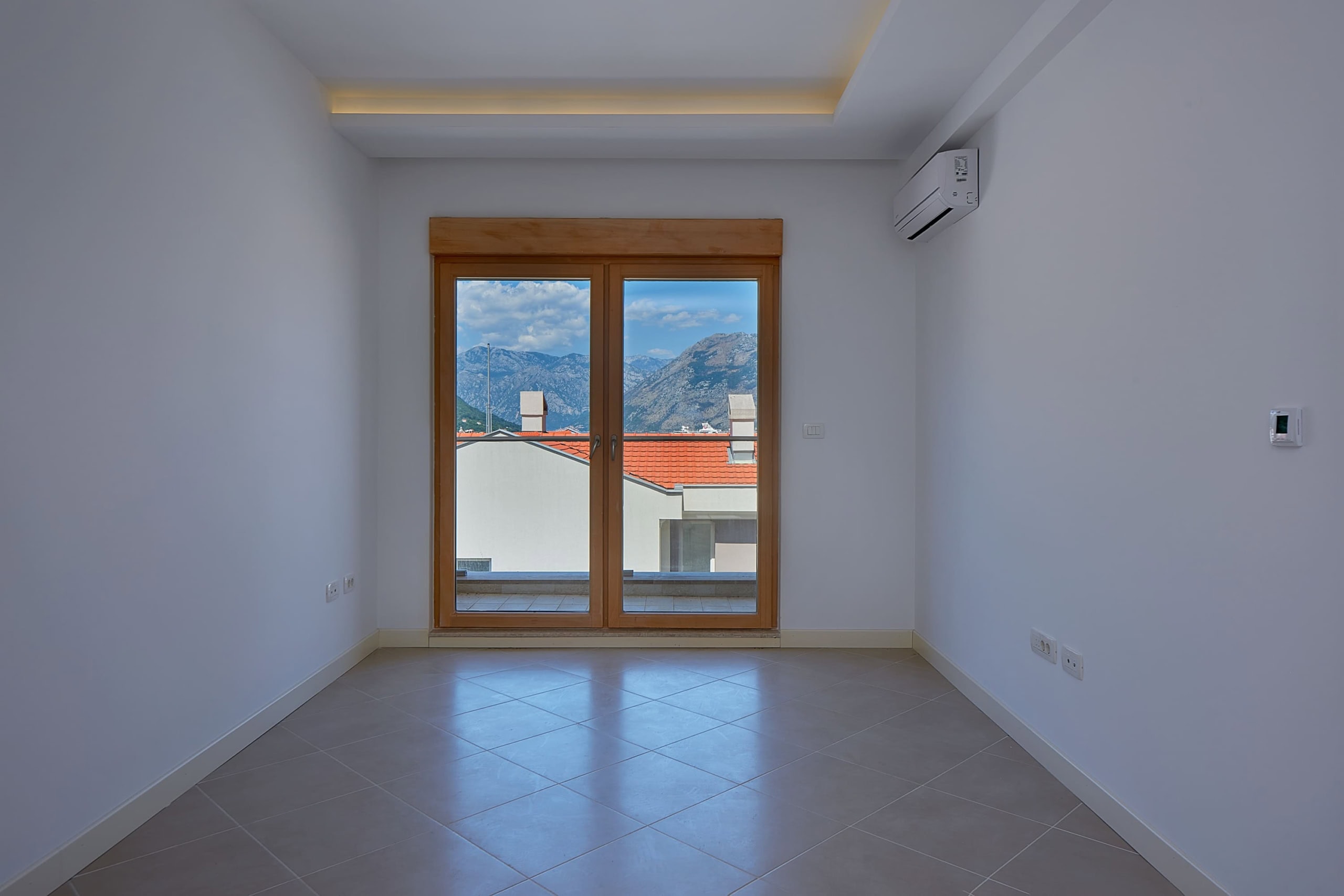 Bright living room in an apartment in Dobrota, Montenegro, with panoramic mountain views and a terrace through a glass door.