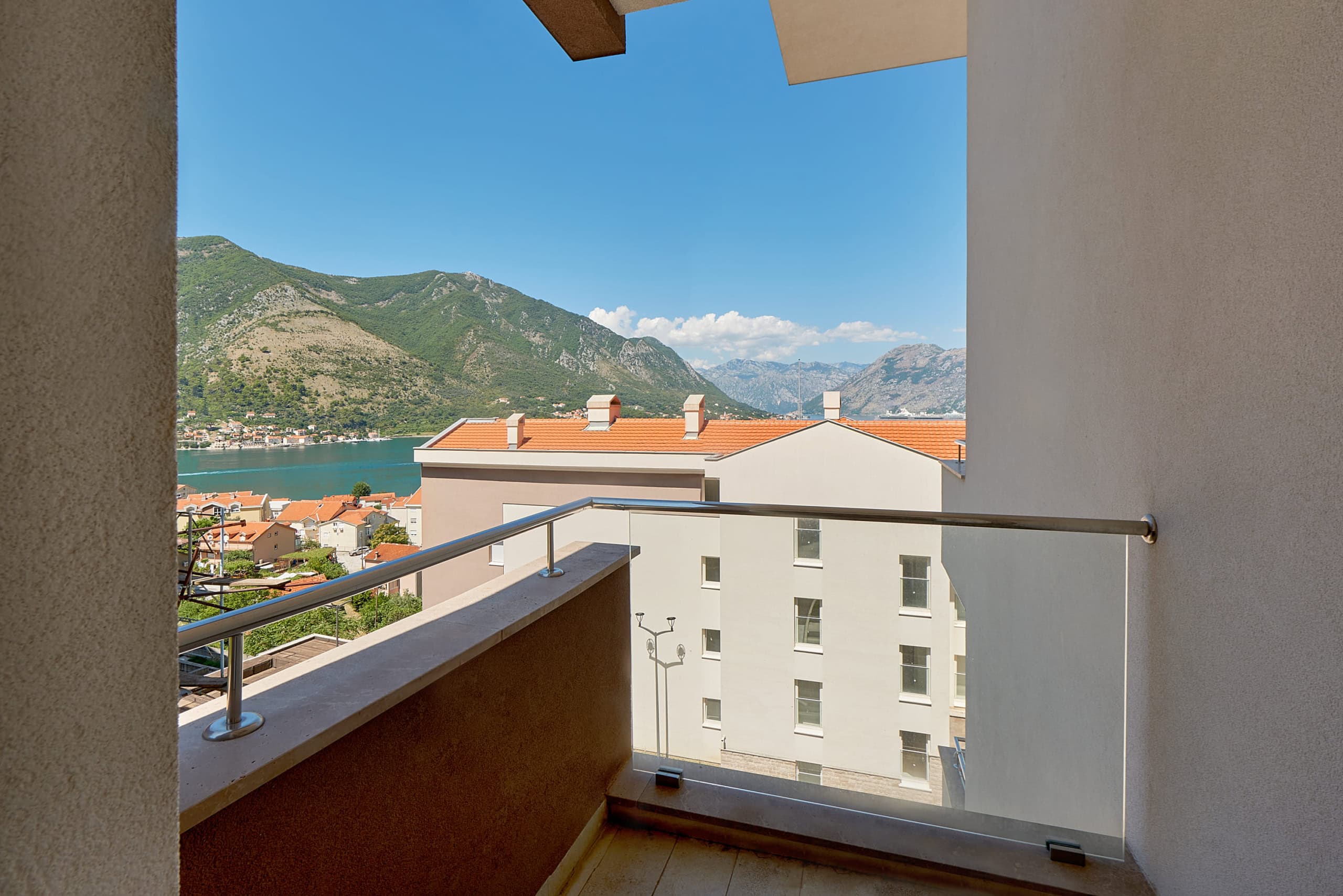View from the apartment balcony in Dobrota, Montenegro: a panorama of the Bay of Kotor, mountains, and the city’s terracotta rooftops.