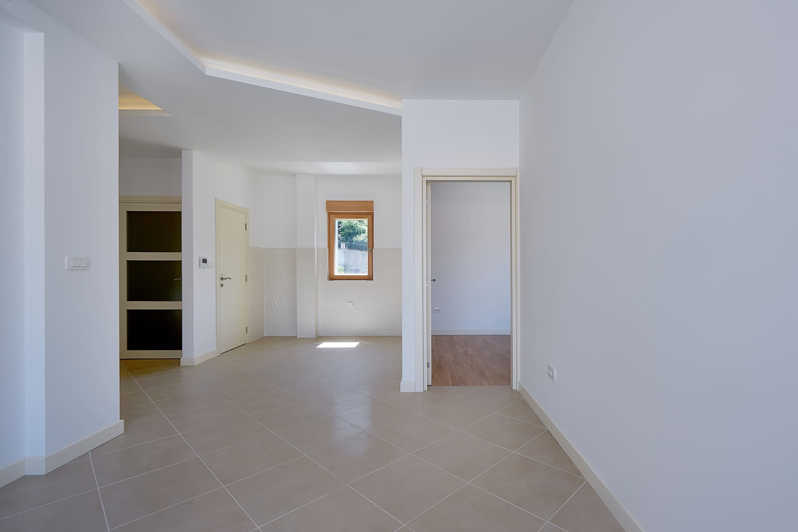 Bright living room in an apartment, Dobrota, Montenegro: white walls, tiled floor, interior doors, and a view from the window.
