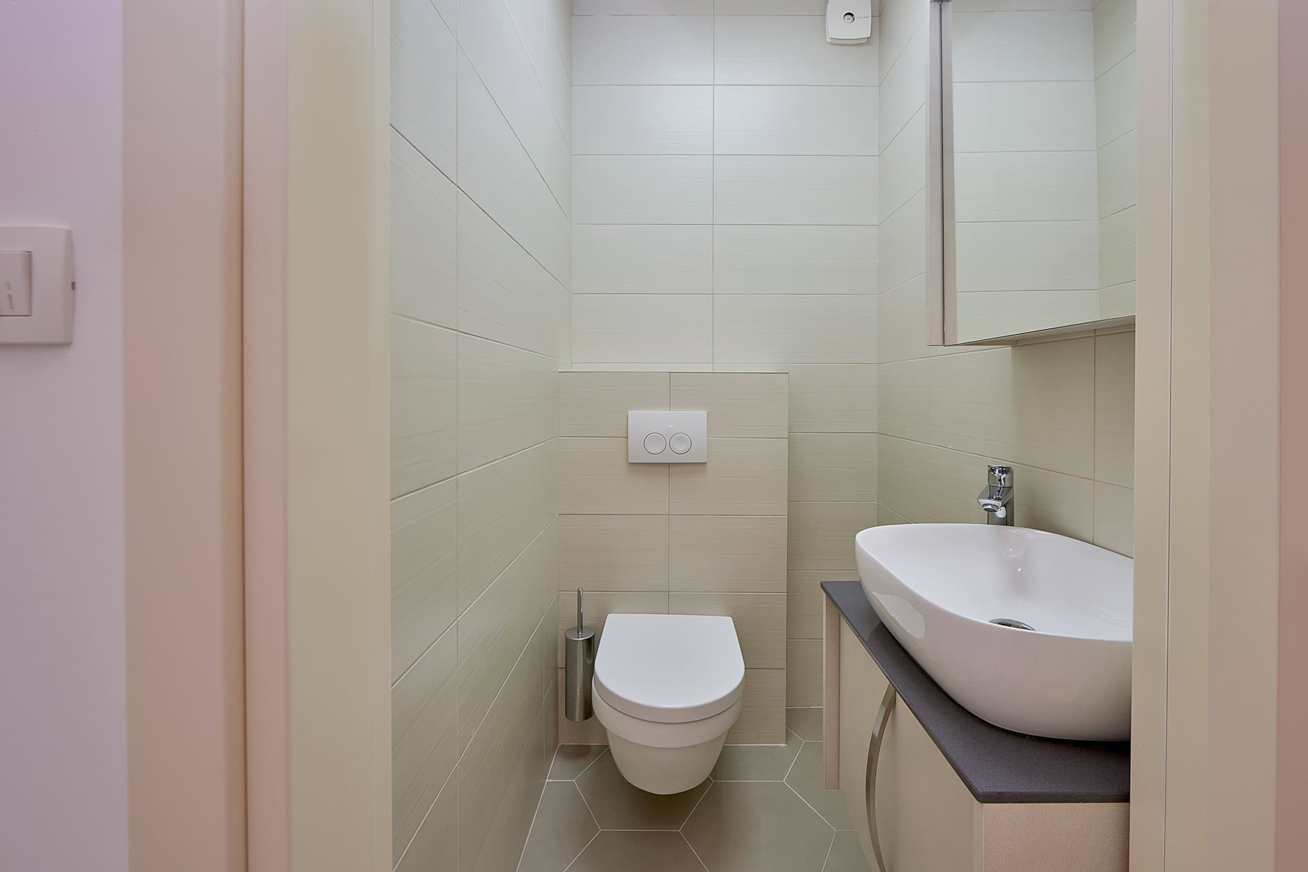 Modern bathroom with wall-mounted toilet and sink in an apartment, Dobrota, Montenegro. Light-colored tile.
