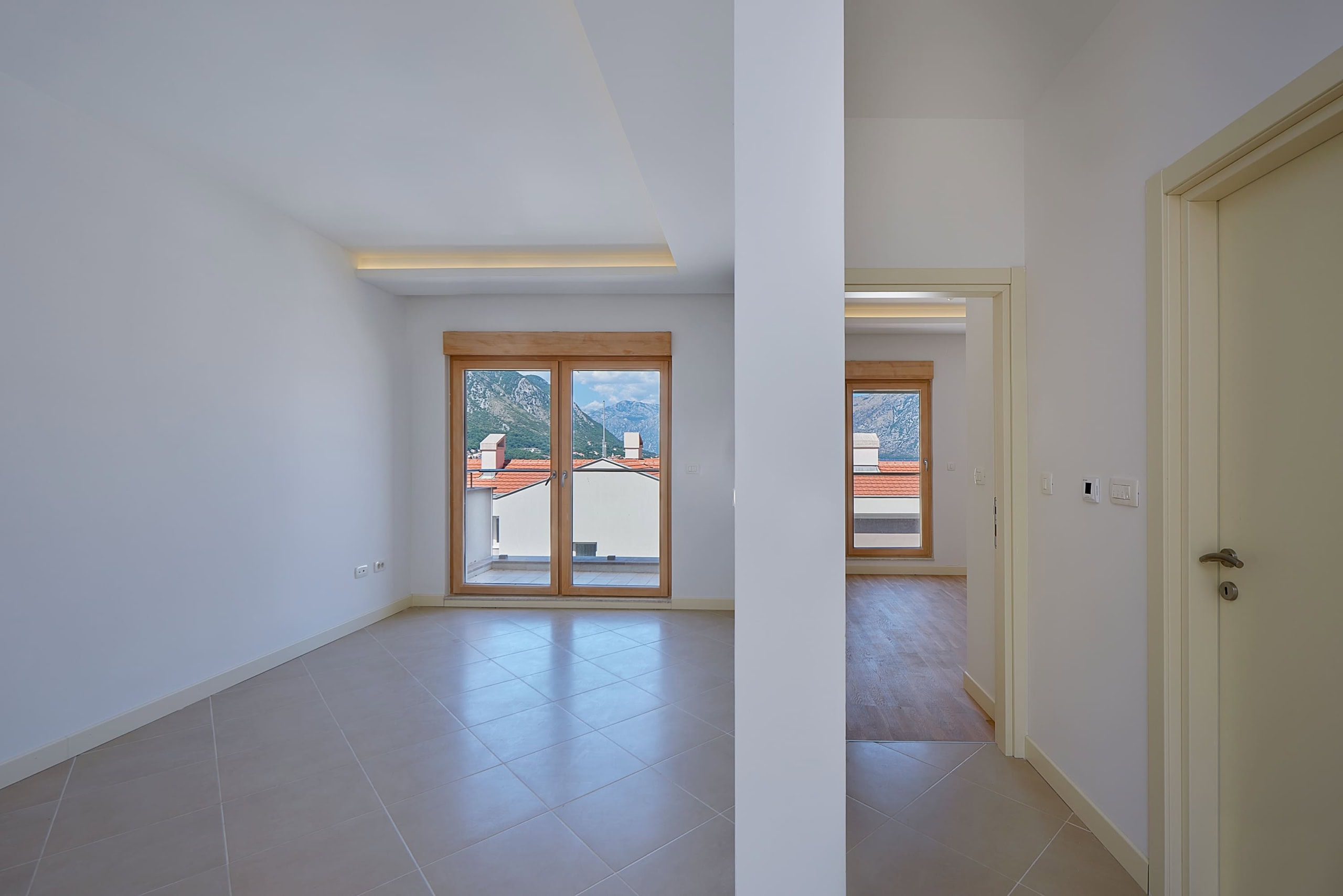 Bright living room in an apartment in Dobrota, Montenegro: tiled floor, panoramic windows with mountain and terrace views.
