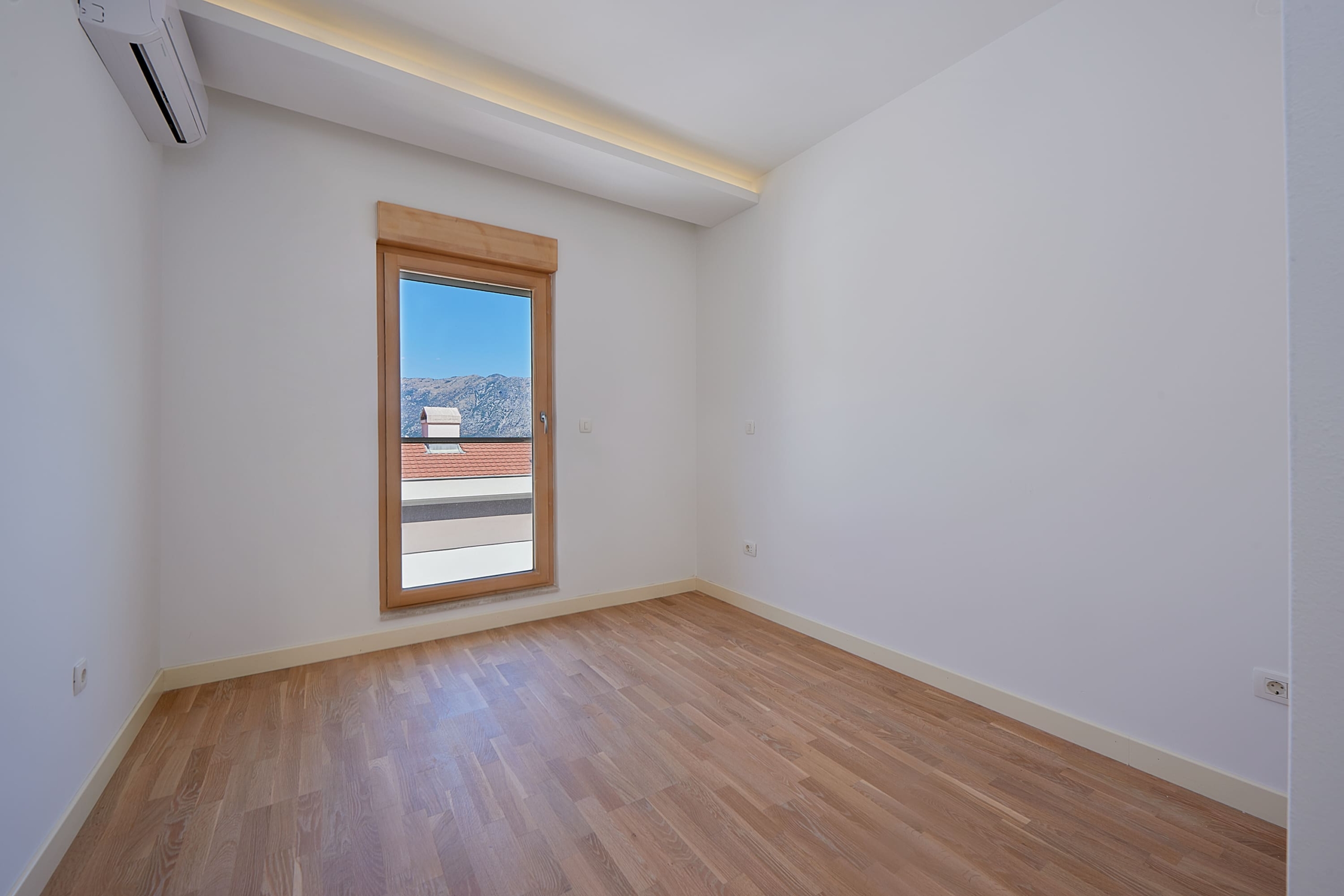 Bright bedroom in an apartment in Dobrota, Montenegro: parquet flooring, air conditioning, and mountain view from the window.
