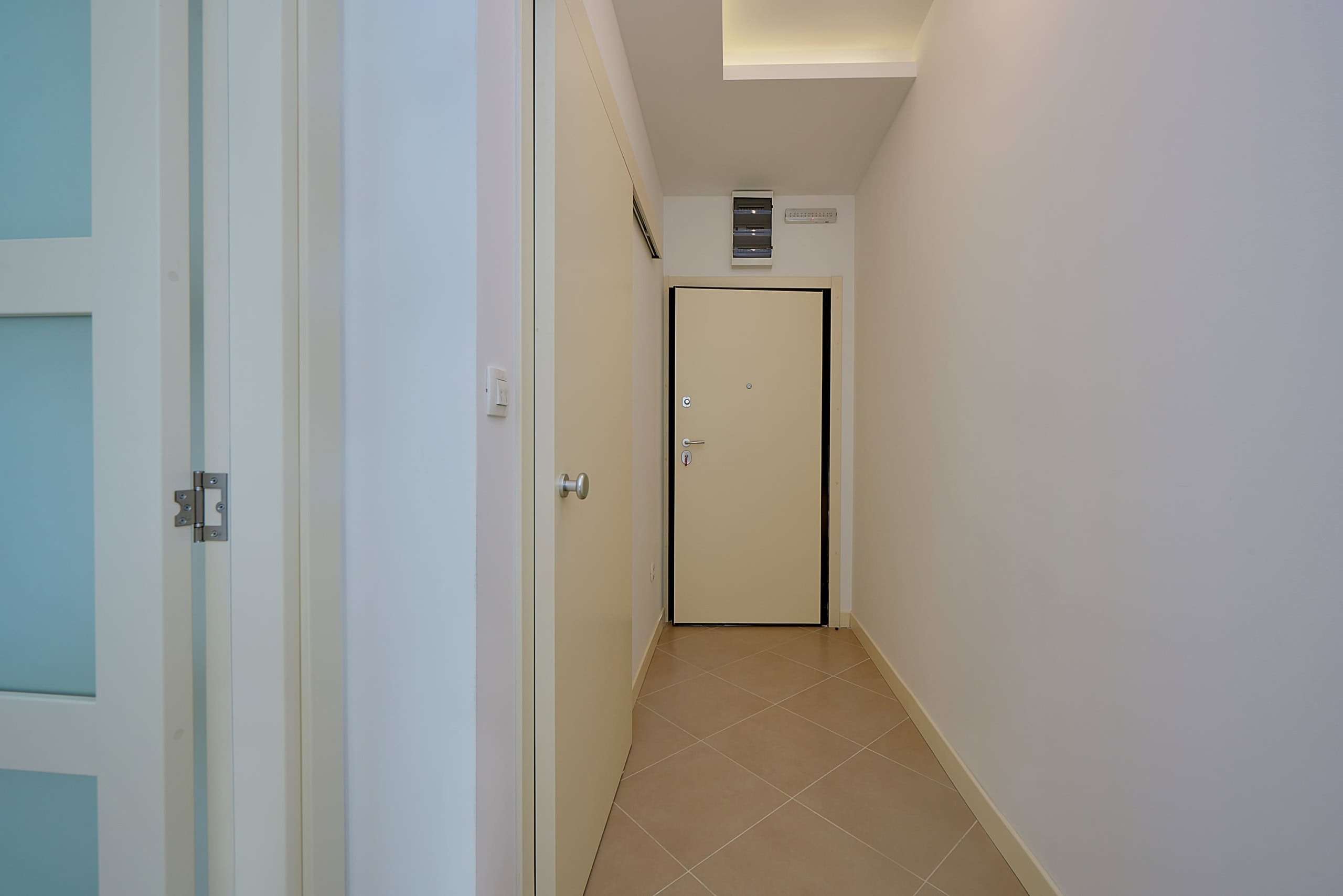 Bright hallway in an apartment, Dobrota, Montenegro: white walls, tiled floor, and a modern-style entrance door.