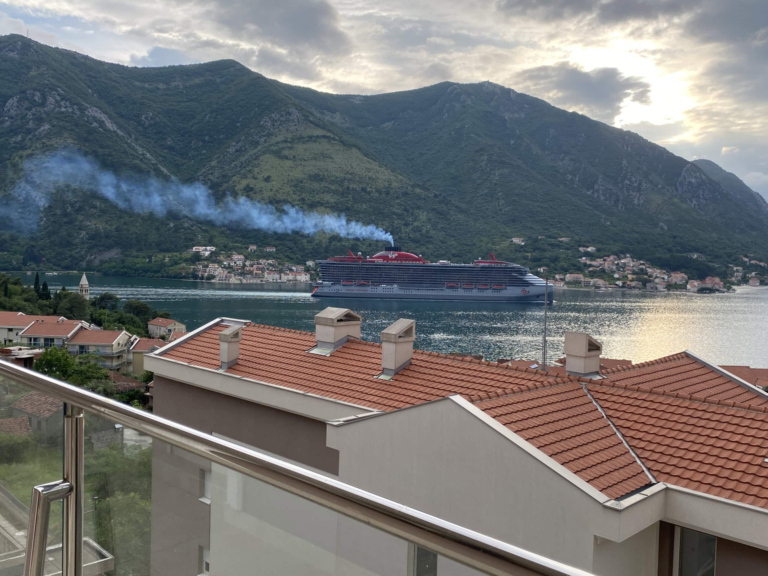 View from the apartment balcony in Dobrota, Montenegro: panoramic view of the Bay of Kotor, a cruise ship, and mountains.