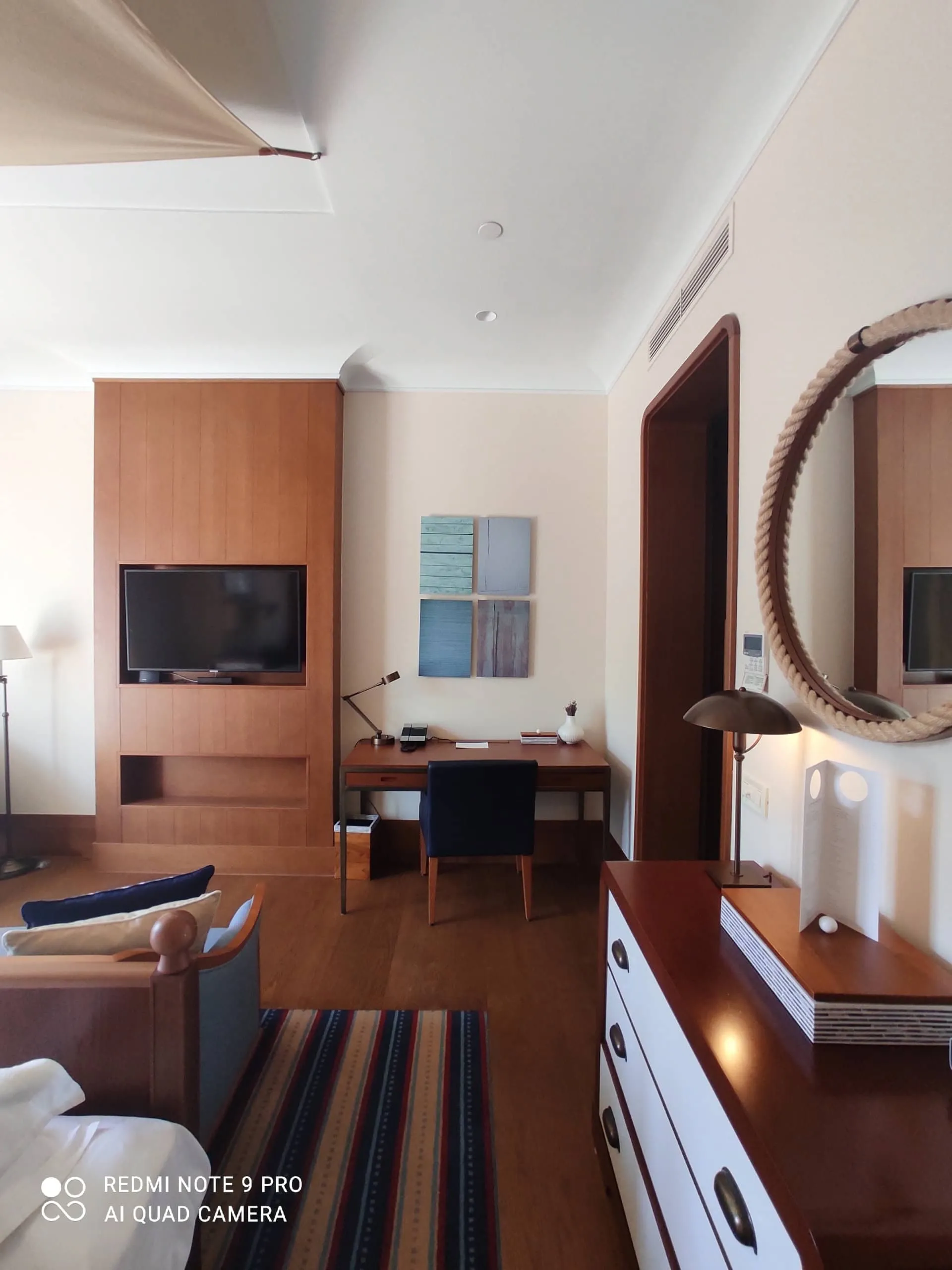 Intérieur d’une chambre moderne dans un appartement à Tivat, Monténégro : mobilier en bois, bureau et miroir rond.