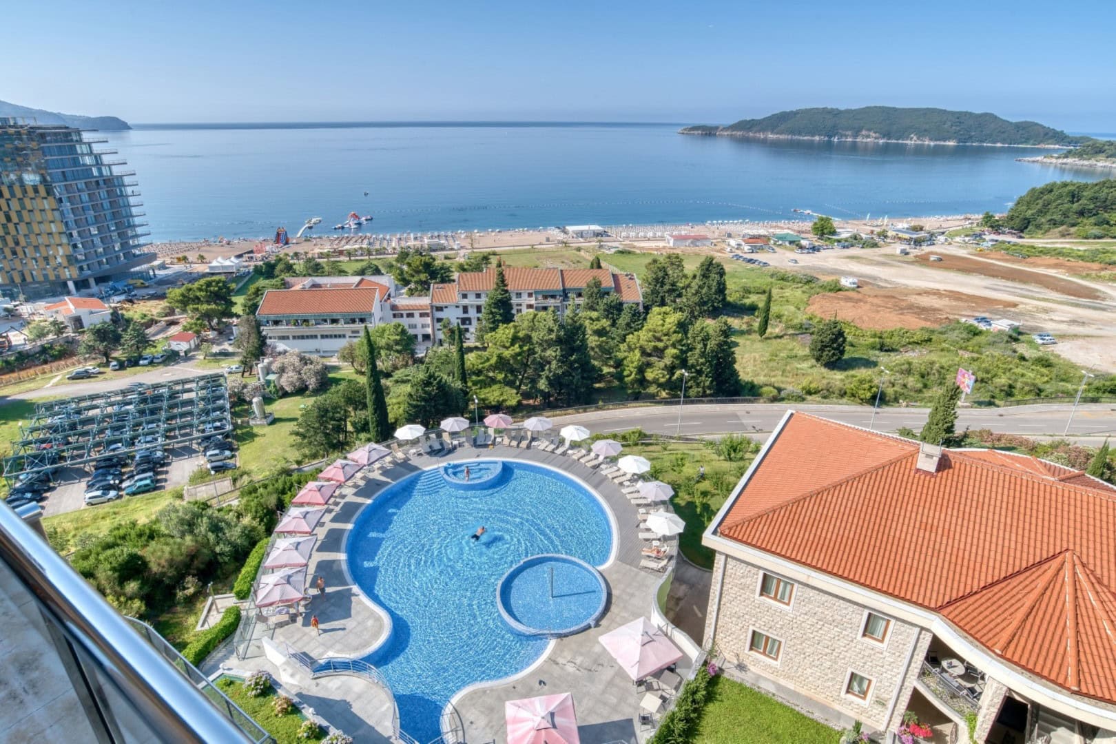Pogled sa balkona penthausa u Bečićima, Crna Gora: otvoreni bazen, plaža i panorama Jadranskog mora.