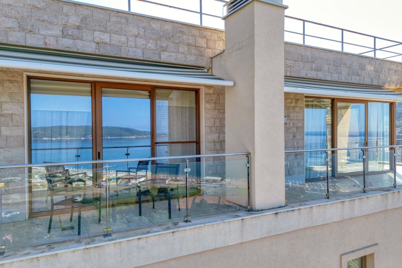 Prostrani balkon penthausa u Bečićima, Crna Gora, sa panoramskim pogledom na more, staklenom ogradom i nameštajem.