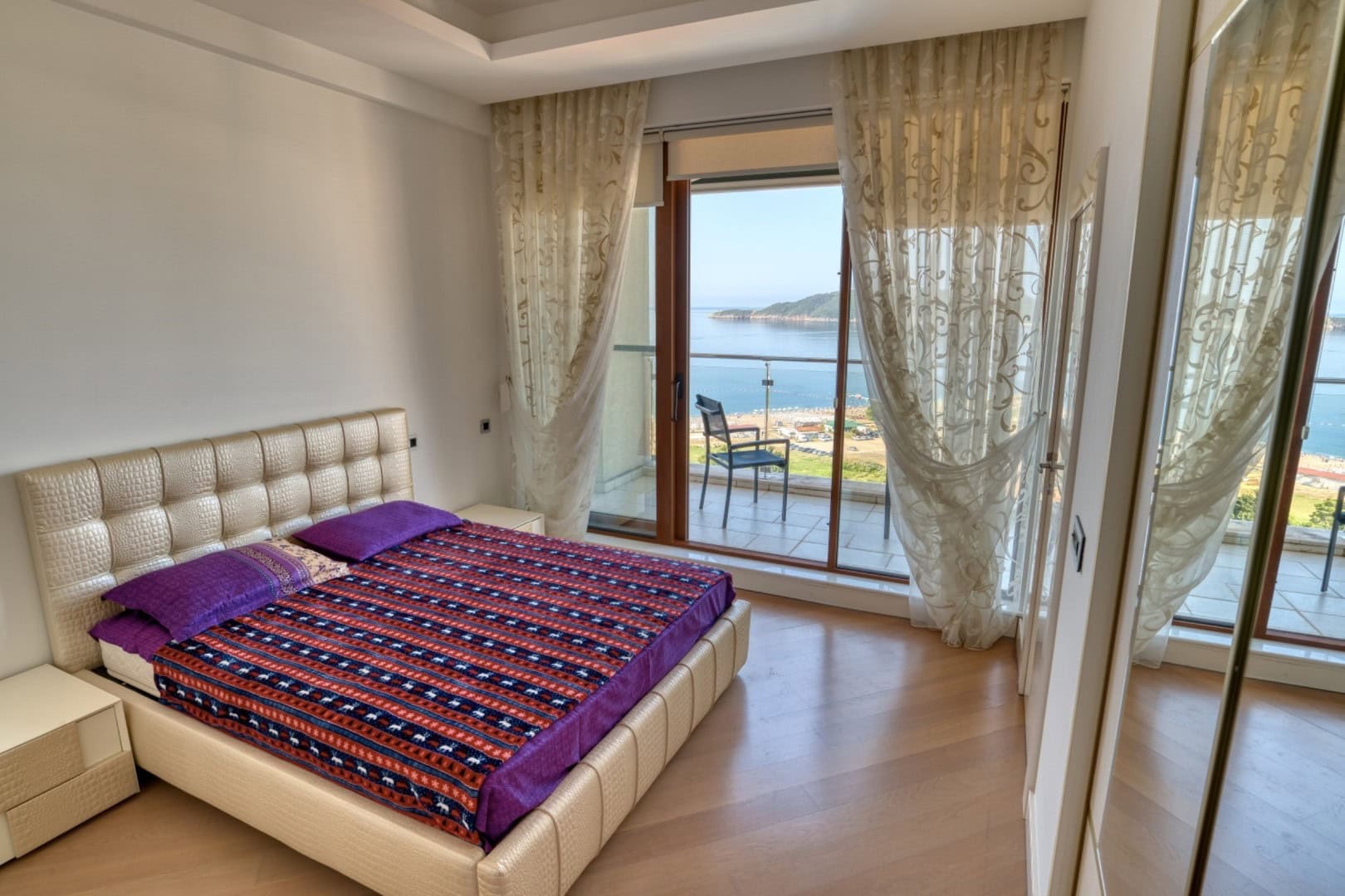 Spavaća soba u penthausu u Bečićima, Crna Gora: bračni krevet, panoramski prozori i balkon sa pogledom na more i plažu.