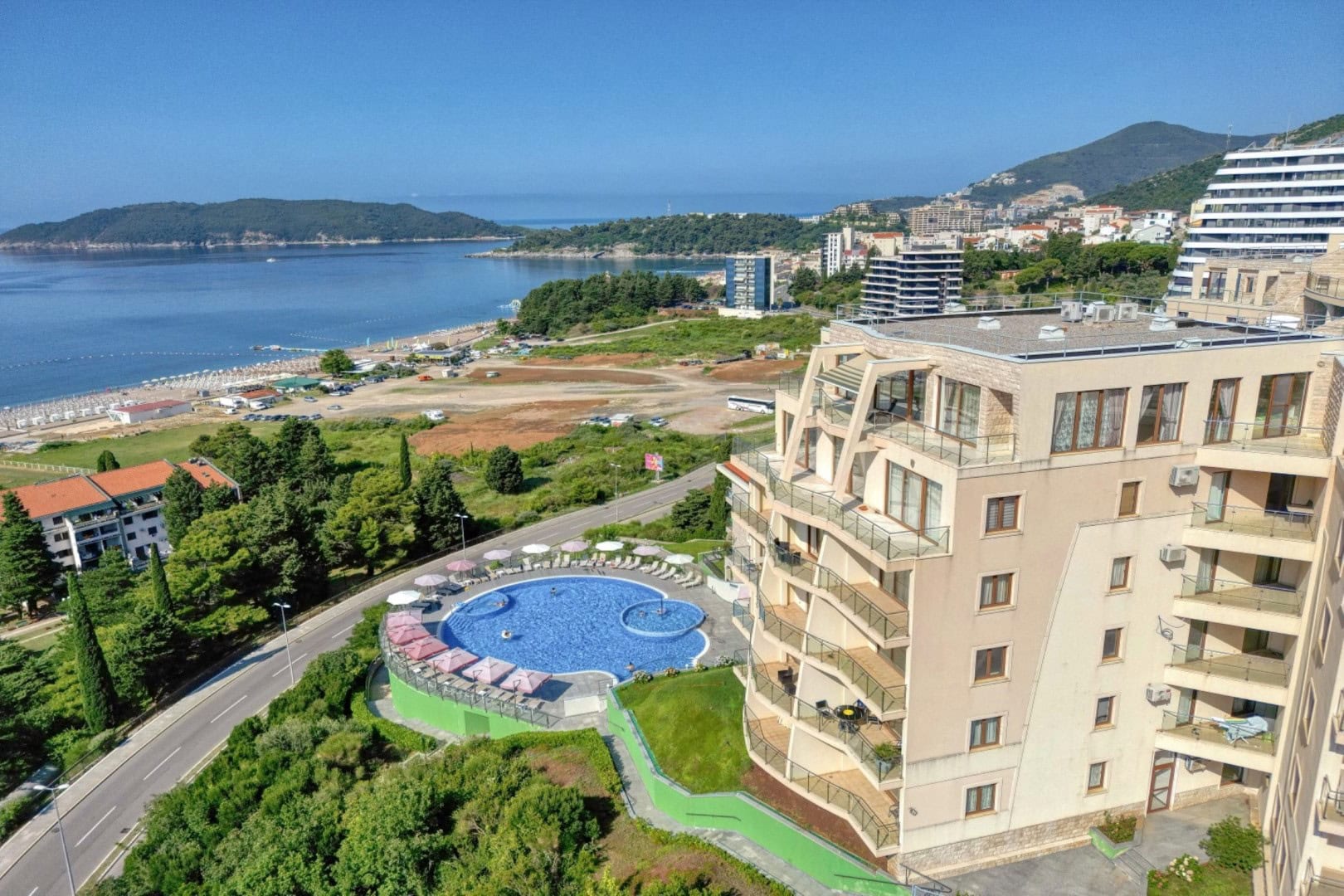 Pogled iz vazduha na stambeni kompleks sa bazenom, plažom i morem u Bečićima, Crna Gora. Penthaus sa panoramskim pogledom na obalu.