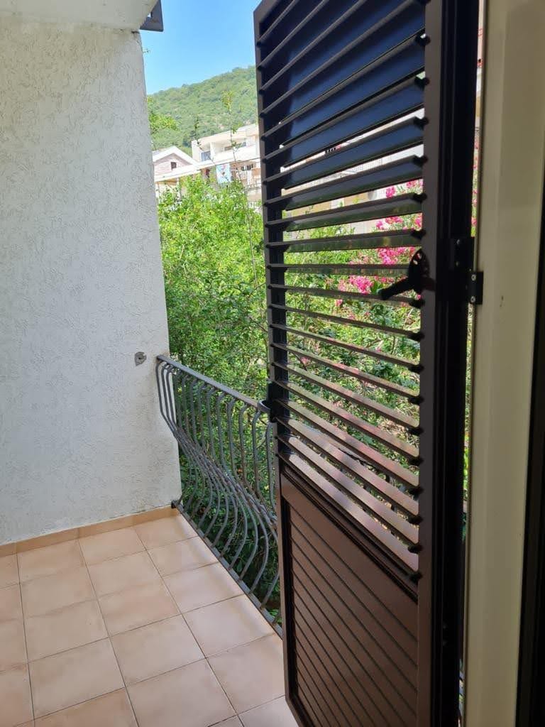 Balkon z kutą balustradą i żaluzjami w mieszkaniu, Petrovac, Czarnogóra: widok na zielone drzewa i góry.