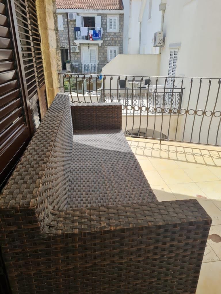 Pleciona sofa na balkonie mieszkania w Petrovacu, Czarnogóra, z widokiem na historyczną architekturę miasta.