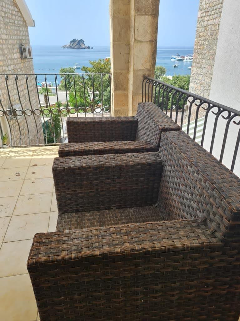 Balkon z plecionymi meblami i panoramicznym widokiem na morze oraz wyspę w mieście Petrovac, Czarnogóra.