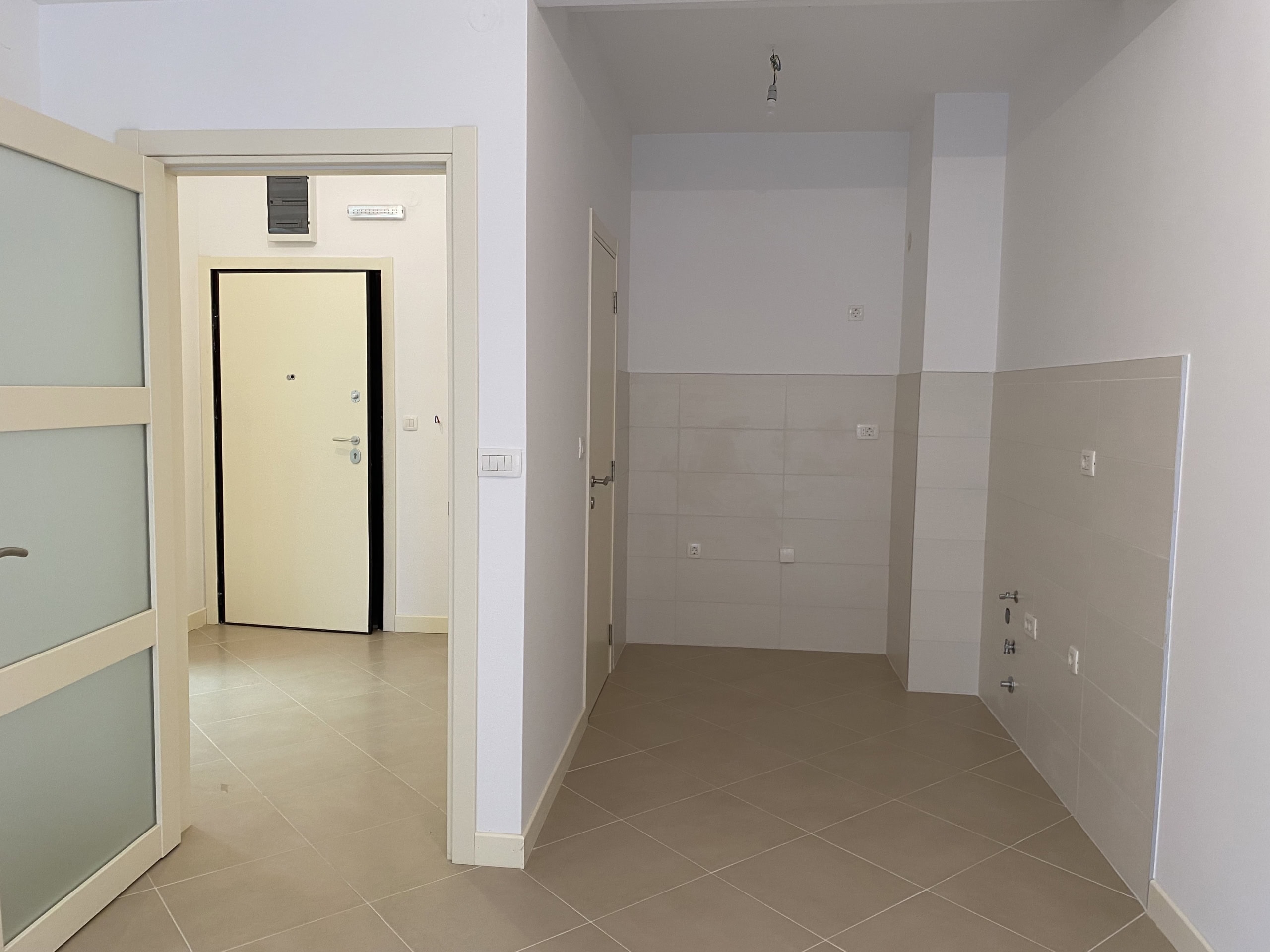 Зона кухни в новой квартире в Доброте, Черногория: светлая плитка, выводы коммуникаций и межкомнатные двери.