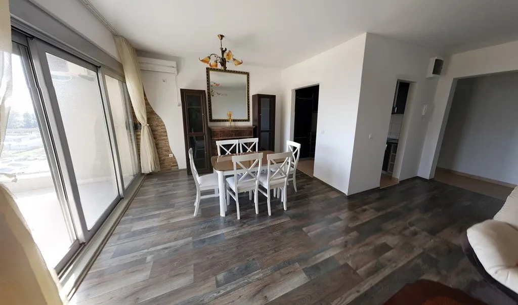 Helles Wohnzimmer mit Essbereich in einer Wohnung in Budva, Montenegro: Panoramafenster, Holzboden und stilvolle Möbel.