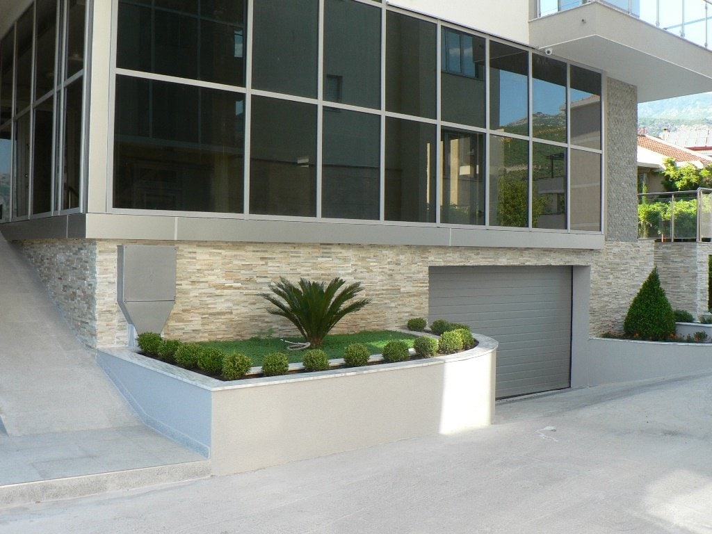 Savremena stambena kuća u Budvi, Crna Gora: panoramsko zastakljenje, kamena obloga i privatna garaža sa uređenim dvorištem.