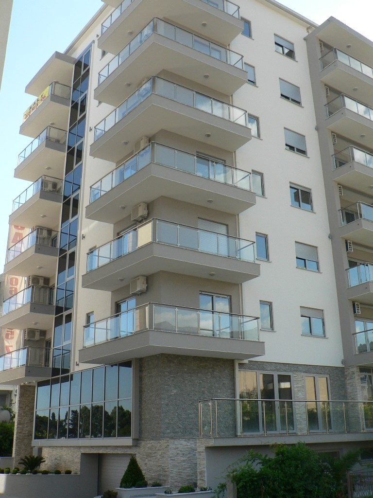 Savremena stambena zgrada u Budvi, Crna Gora: fasada sa panoramskim prozorima, staklenim balkonima i kamenim oblogama.
