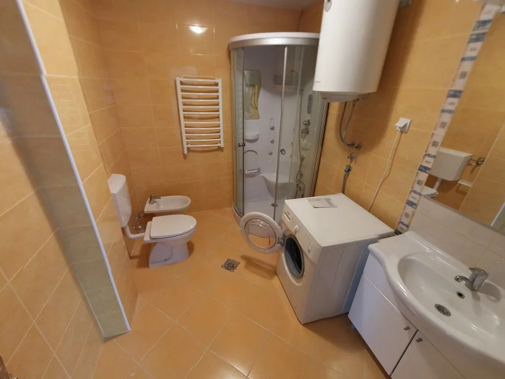 Badezimmer in einer Wohnung in Budva, Montenegro: Duschkabine, Waschmaschine, Bidet und helle Fliesen.