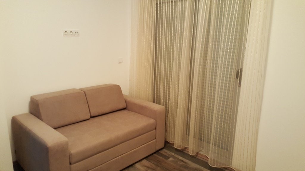 Udobna dnevna soba sa bež kaučem i panoramskim prozorom u stanu u Budvi, Crna Gora. Svetao enterijer sa laminatom.