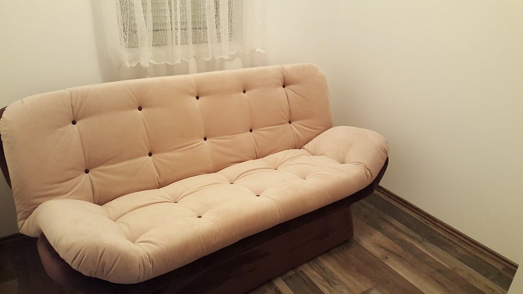Svetla sofa u dnevnoj sobi stana u Budvi, Crna Gora: enterijer sa laminatom i belim zidovima.